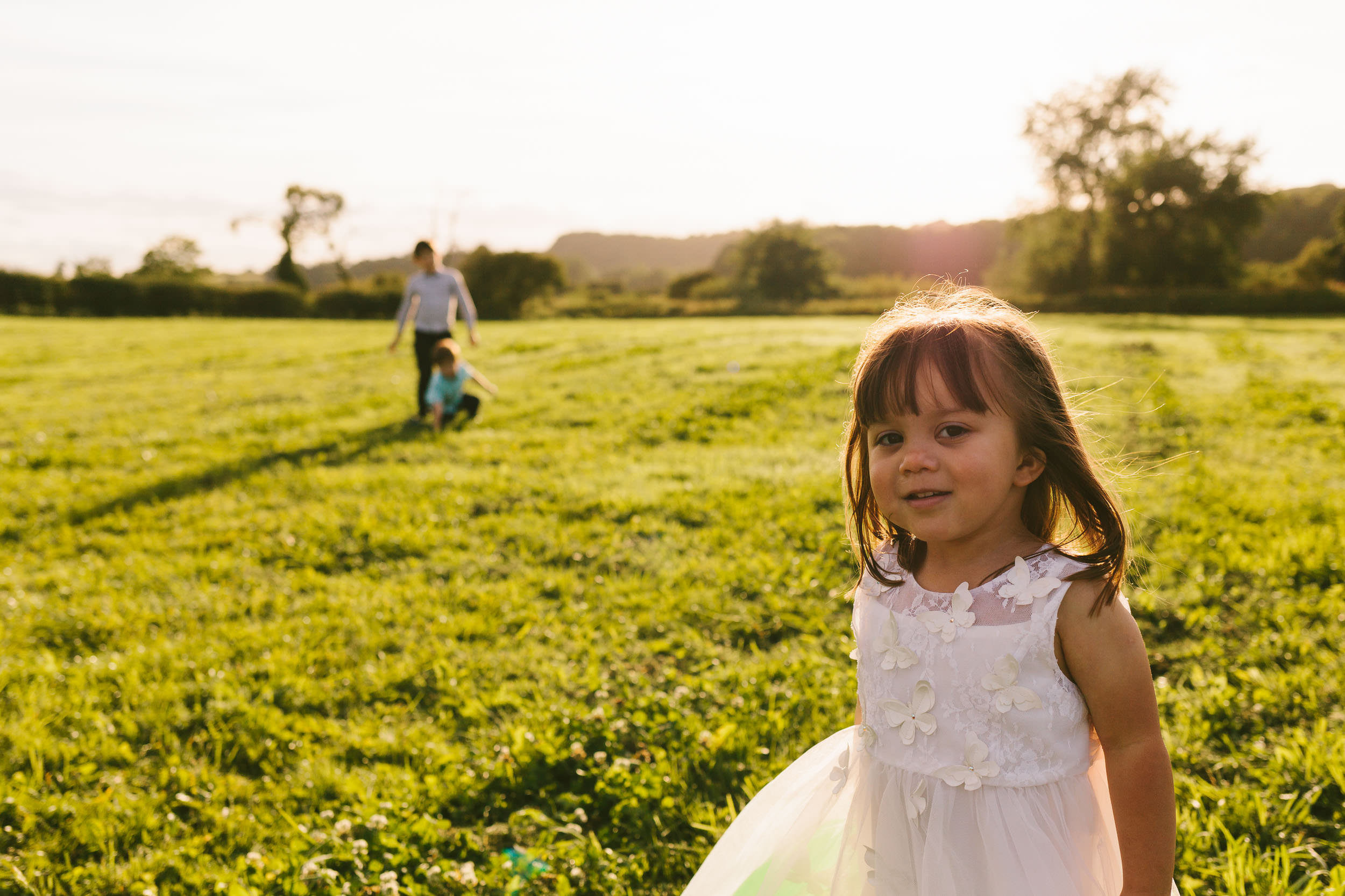 Bride and grooms daughter plays in fields under warm sunlight