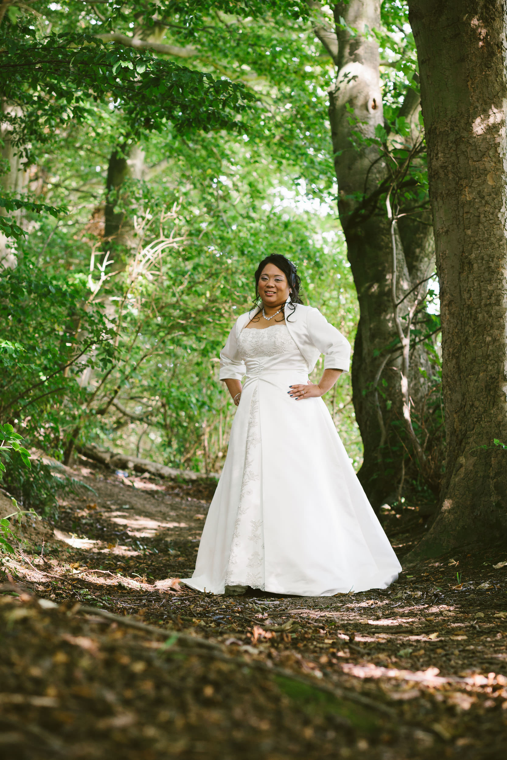 Bride poses on woodland path in dappled light