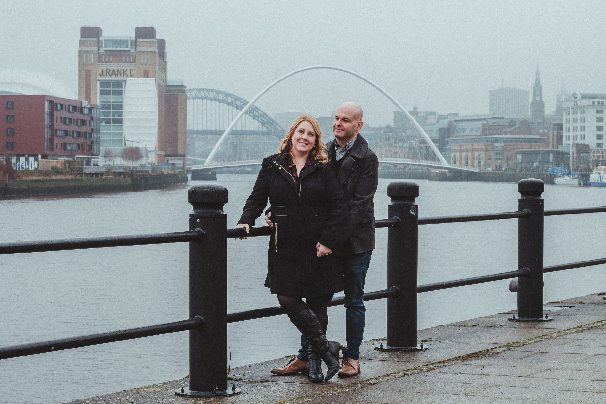 Engaged couple pose on foggy Quayside with Baltic and bridges in background