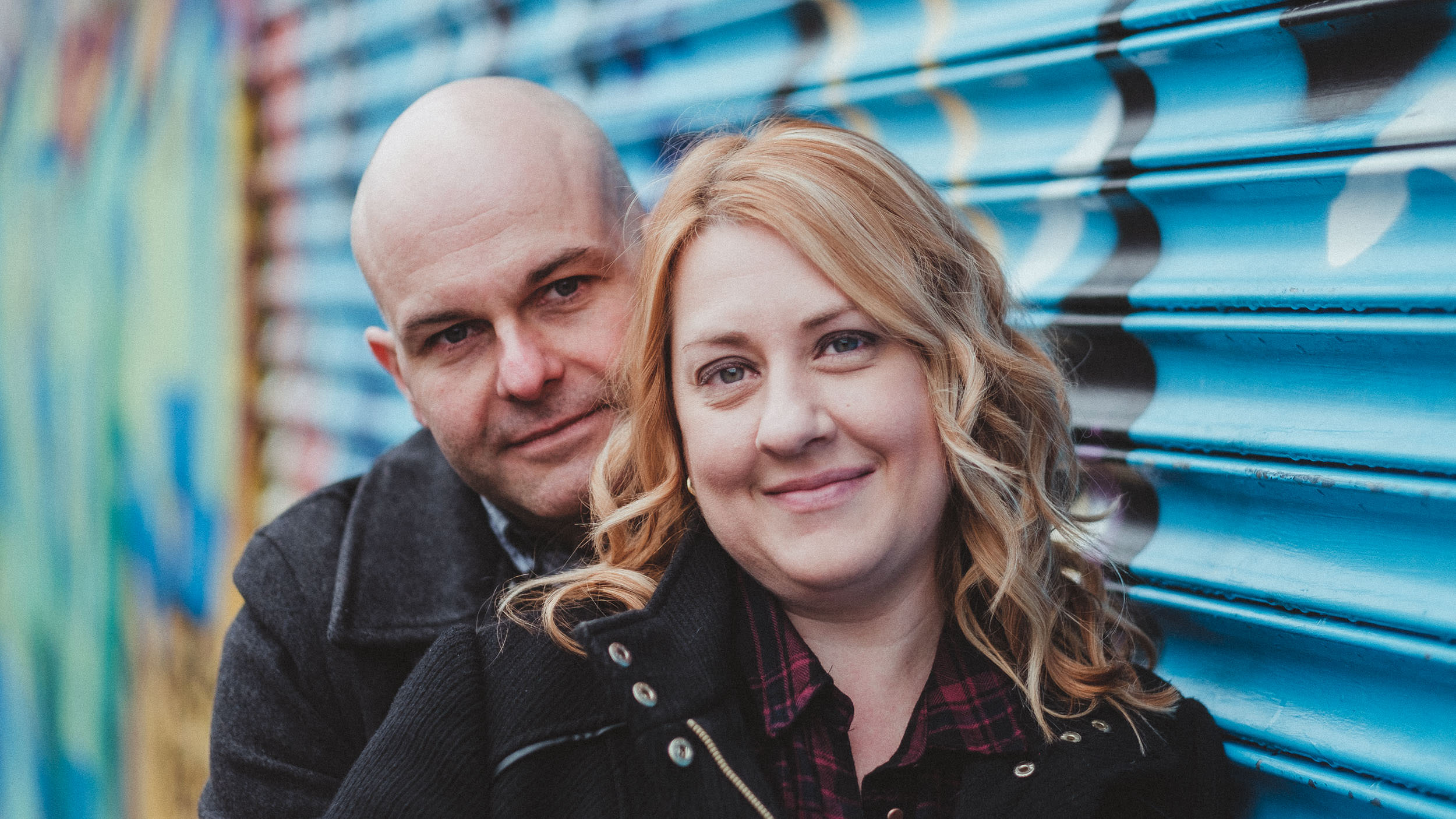 Close up of a couple standing in front of graffiti covered shutters