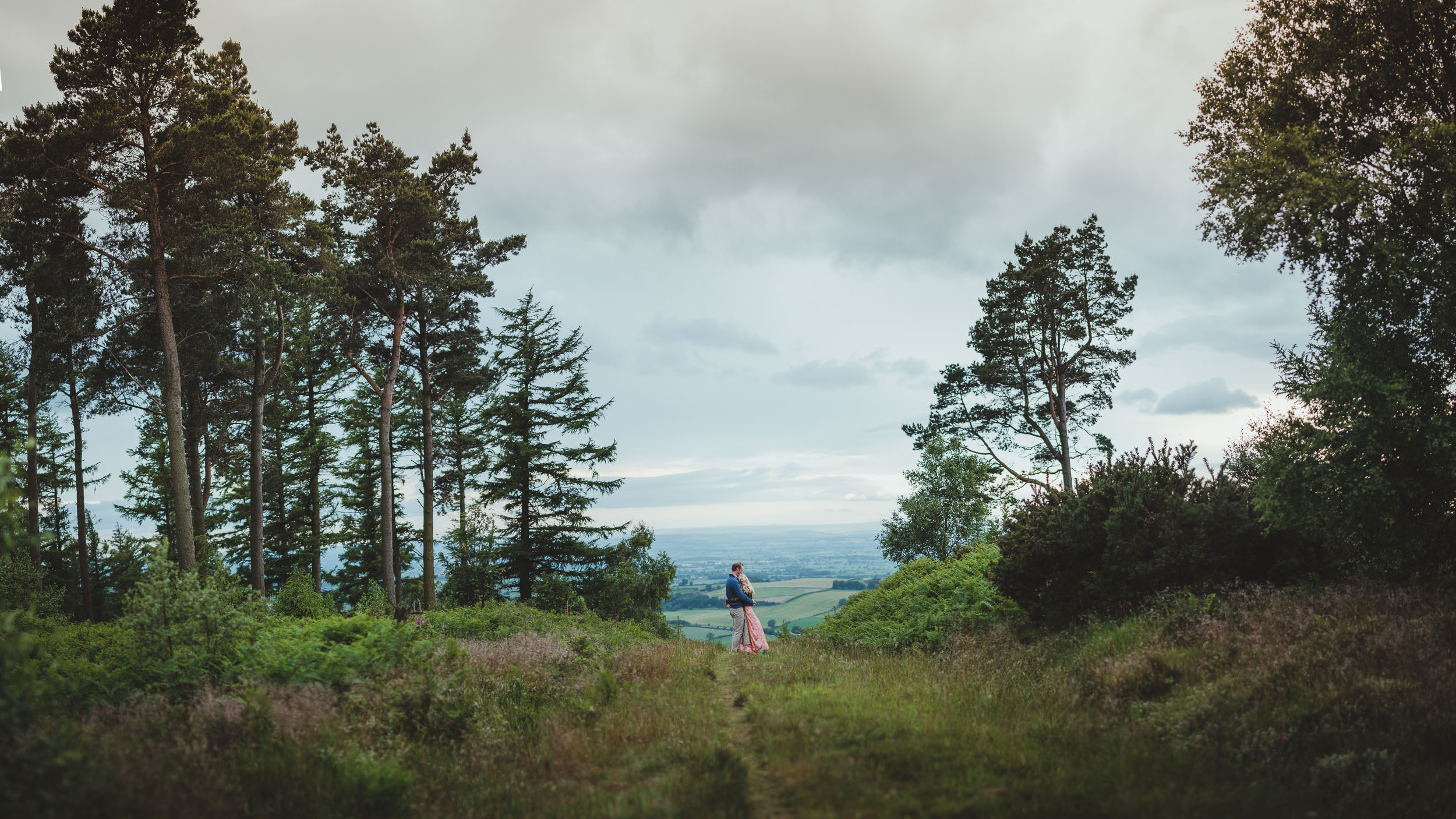 A wide panorama of a country path high in the Yorkshire hills with an engaged couple cuddling