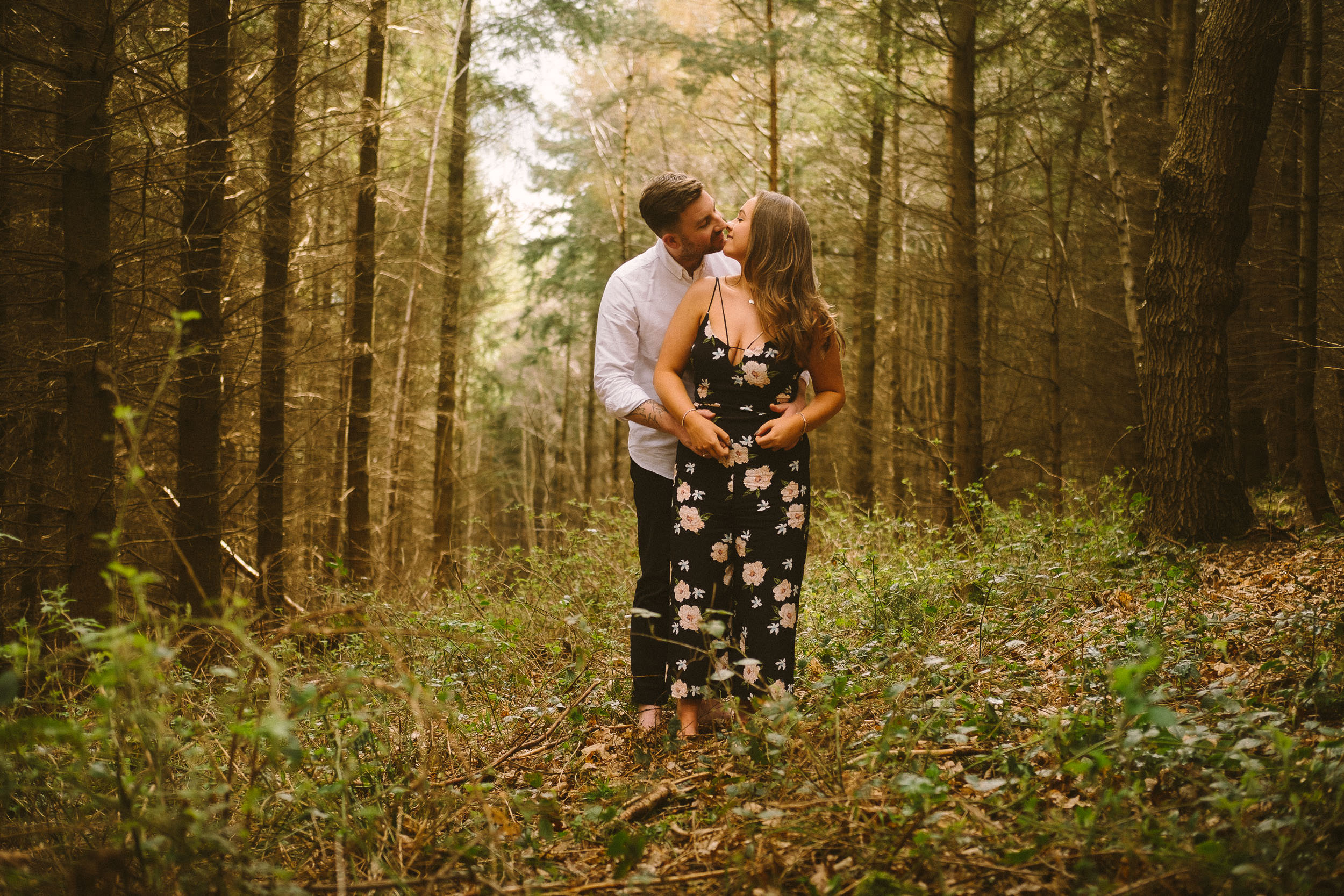 An engaged couple kiss while standing in wild woodland