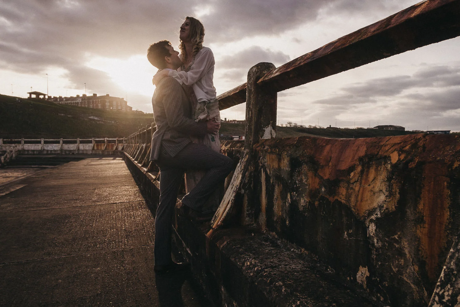 Dramatic photo of couple embracing near rusty fence with strong sunlight from behind