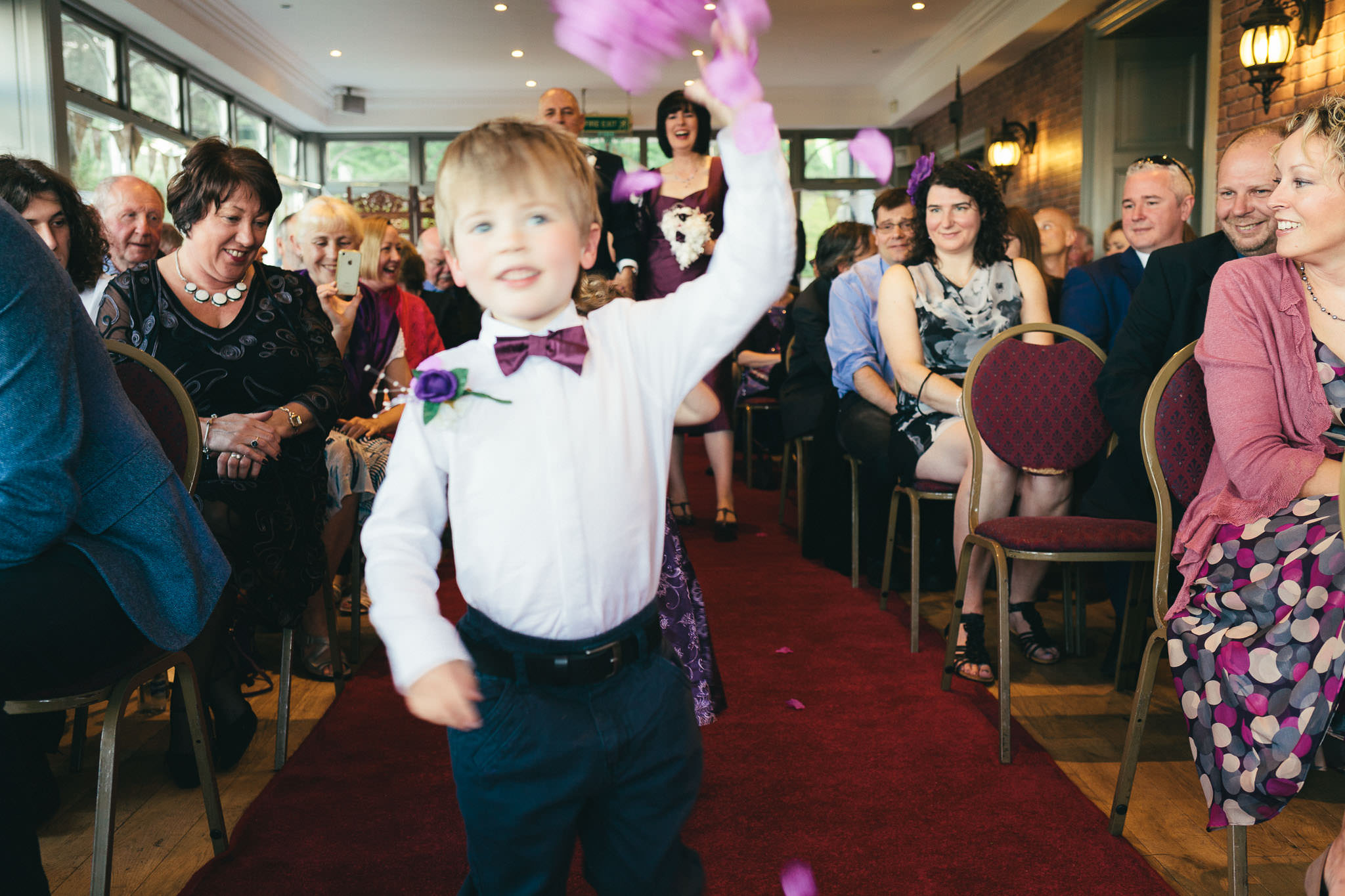 Page boy throws flower petals as bride and groom arrive at ceremony