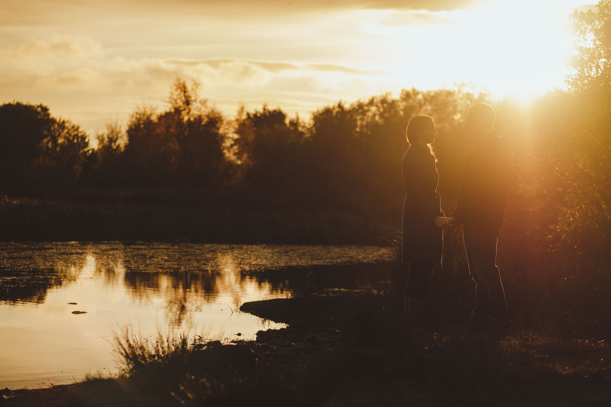 Sun drenched photo of an engaged couple holding hands near a lake