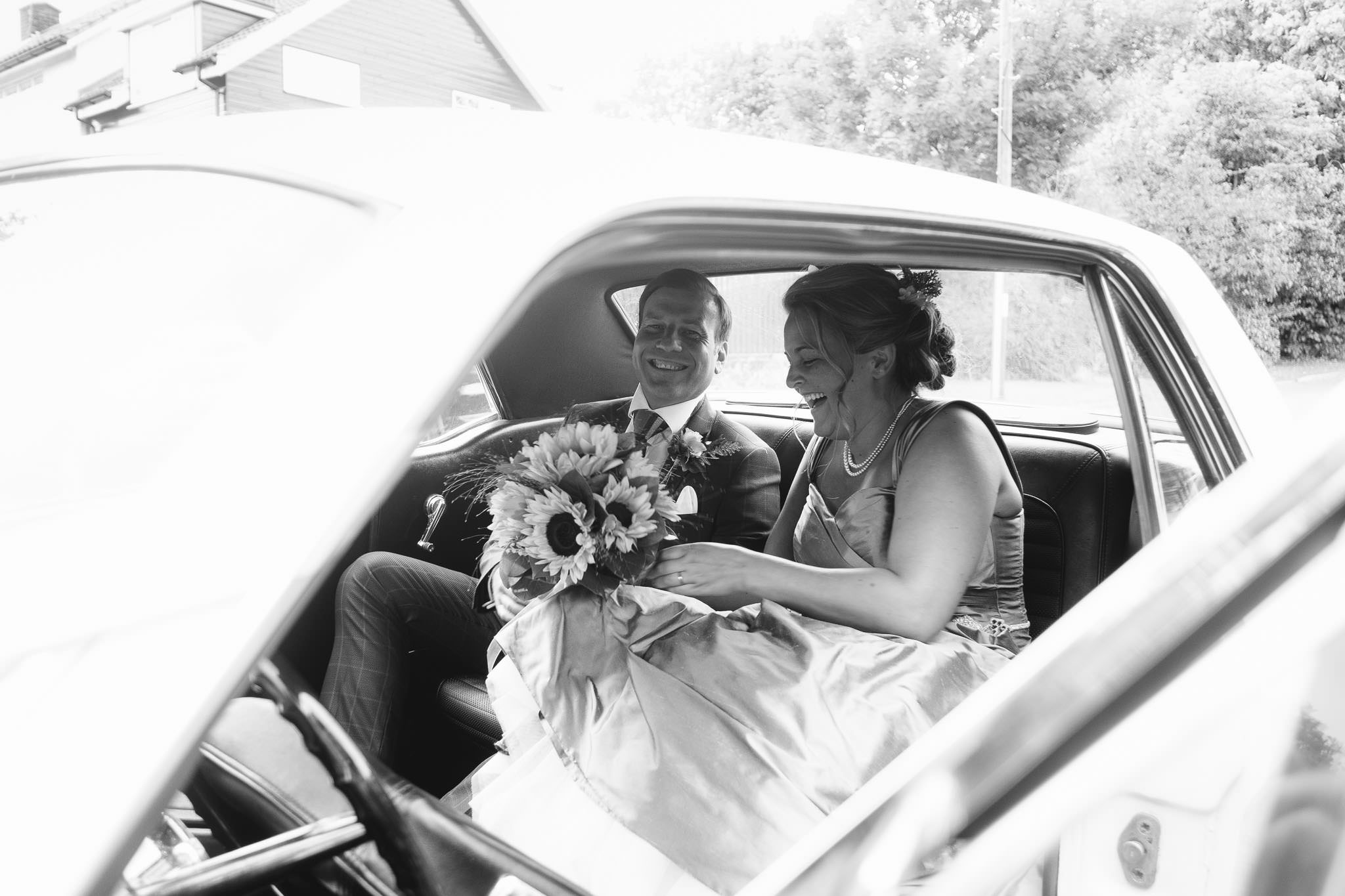 A black and white photo of the bride and groom getting in the car after their wedding ceremony