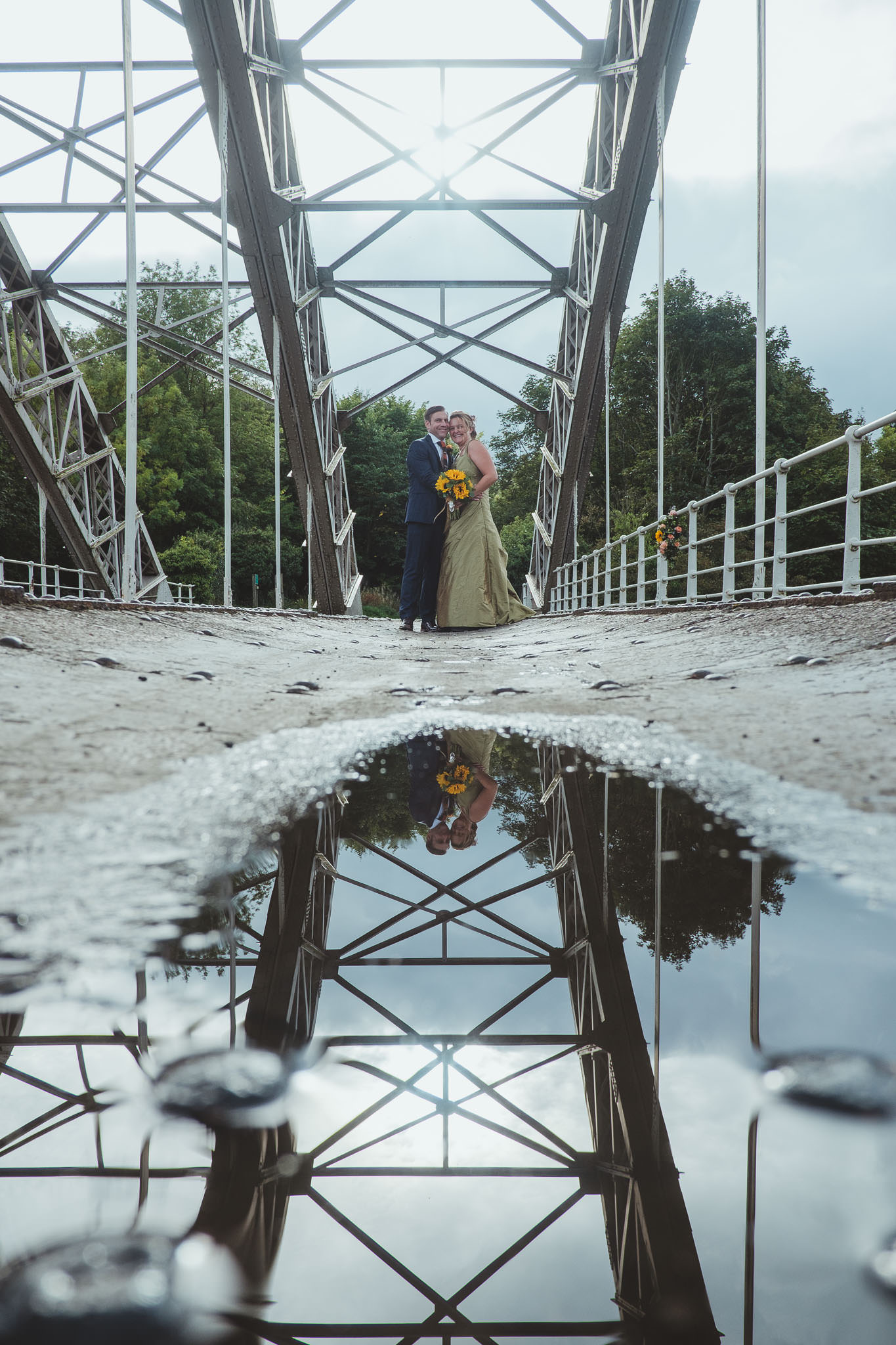 Bride and groom reflected in a puddle on a bridge