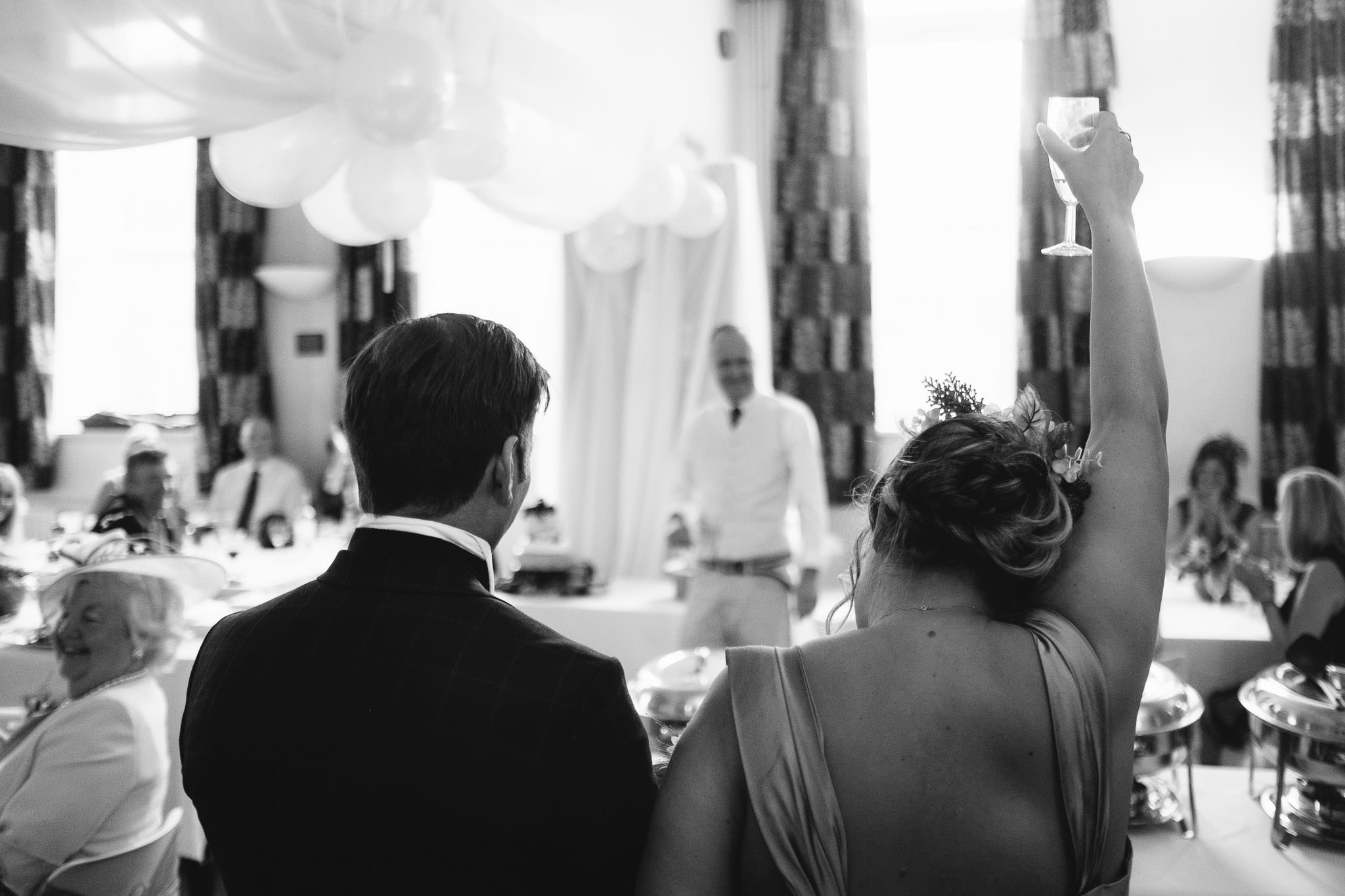 A black and white photo of the bride and groom toasting a wedding speech