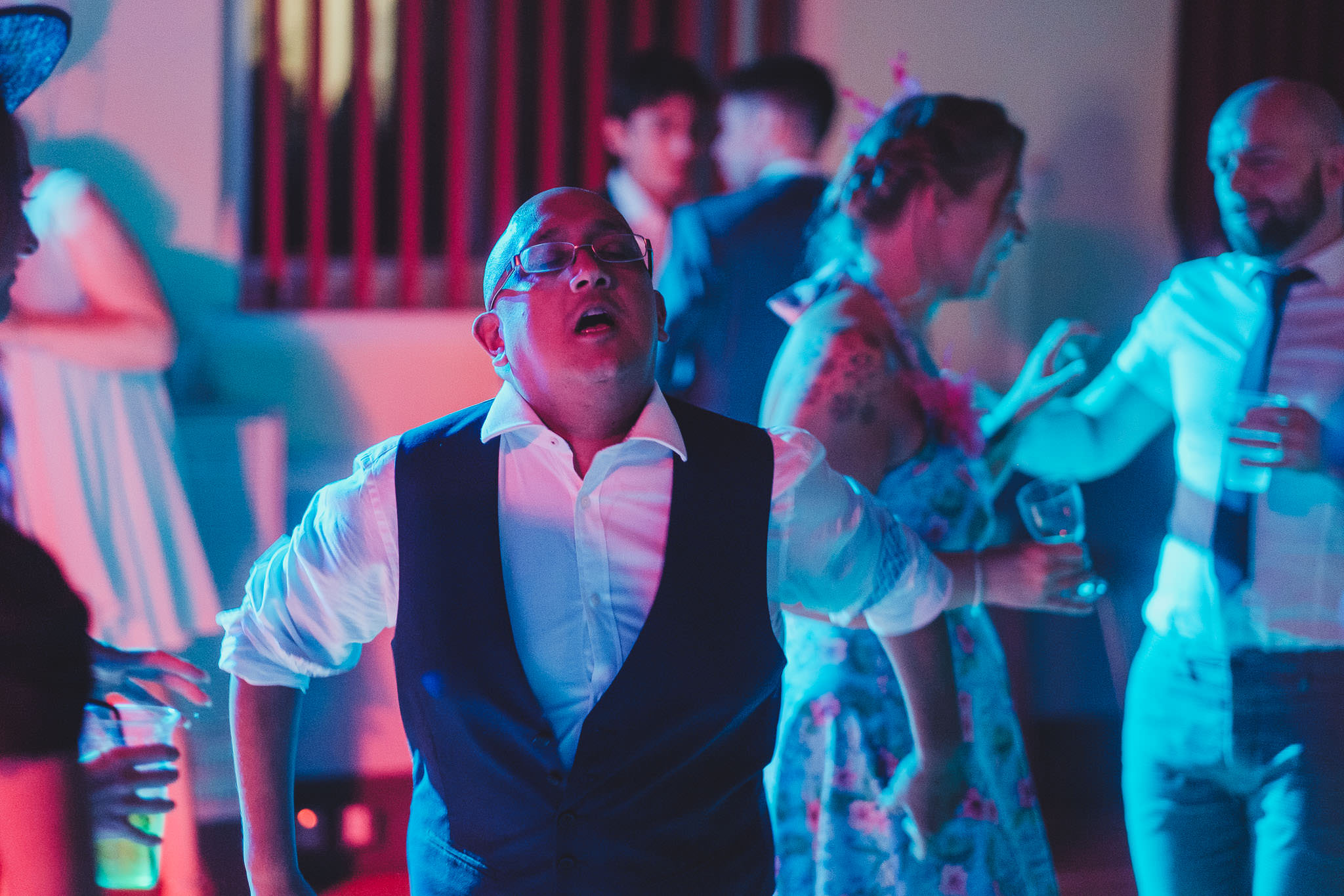 A wedding guest dancing and singing bathed in colourful light