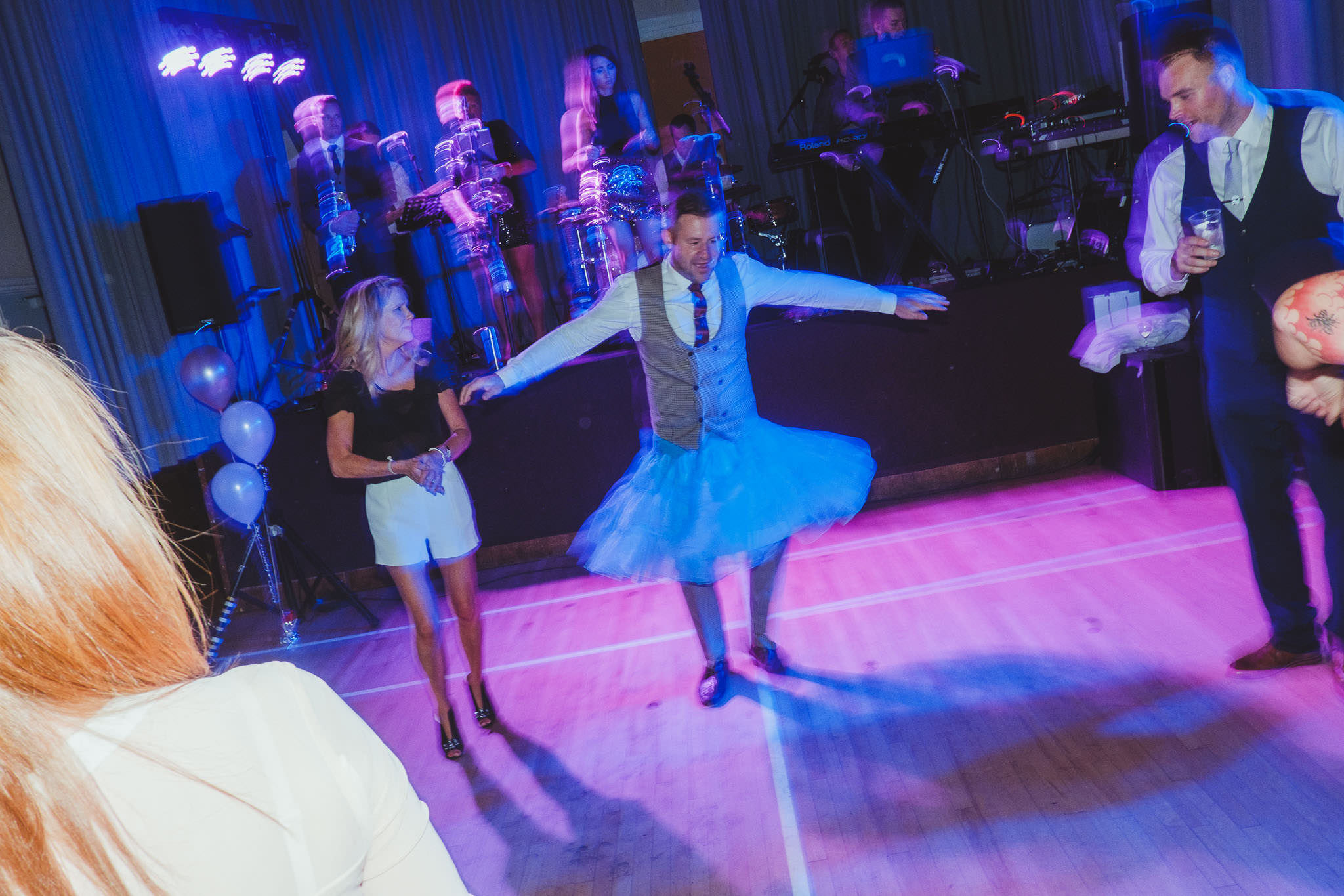 A male wedding guest dances in a blue tutu