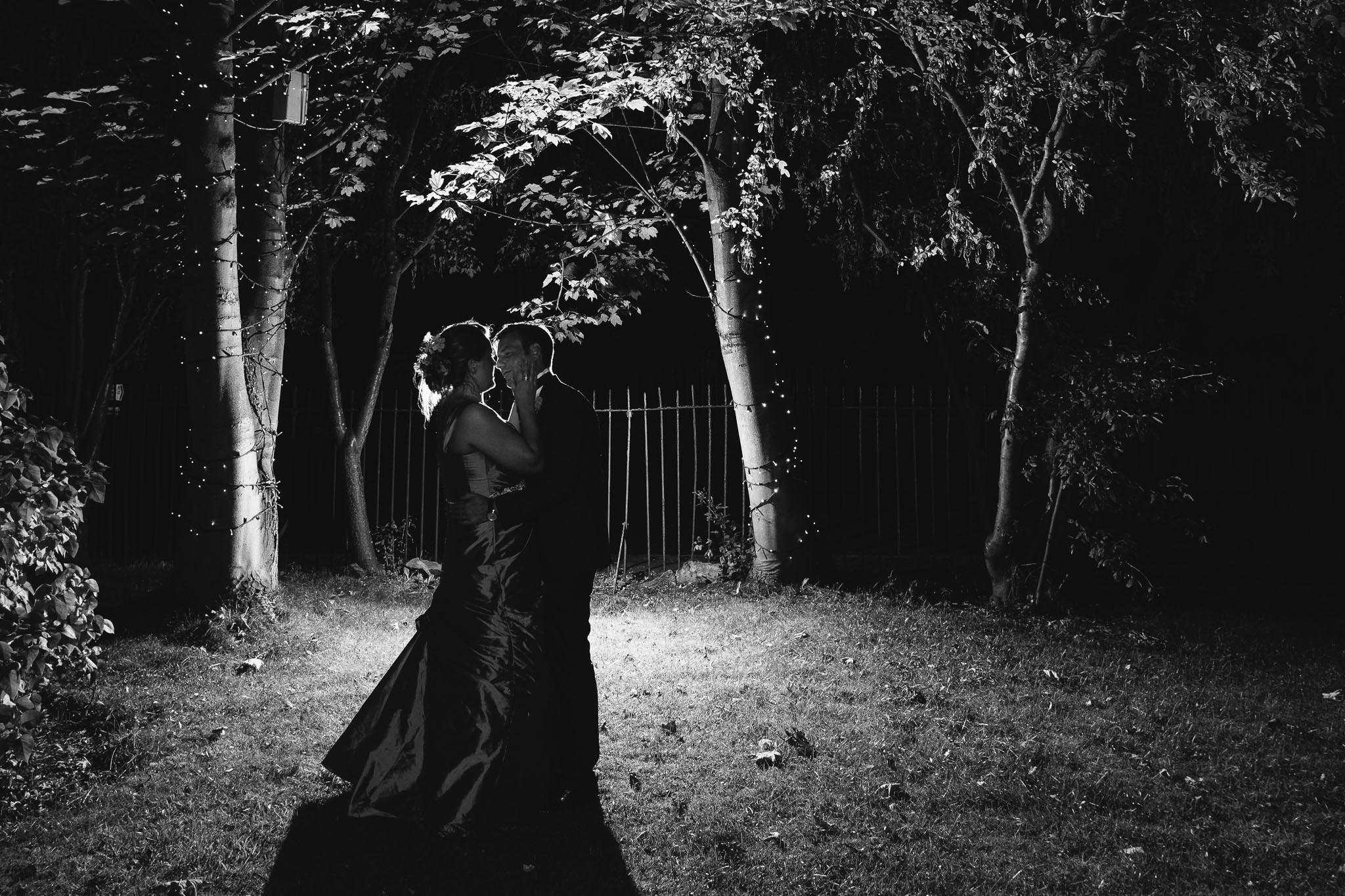 A romantic black and white photo of the bride and groom embracing in the grounds of Wylam Institute at night