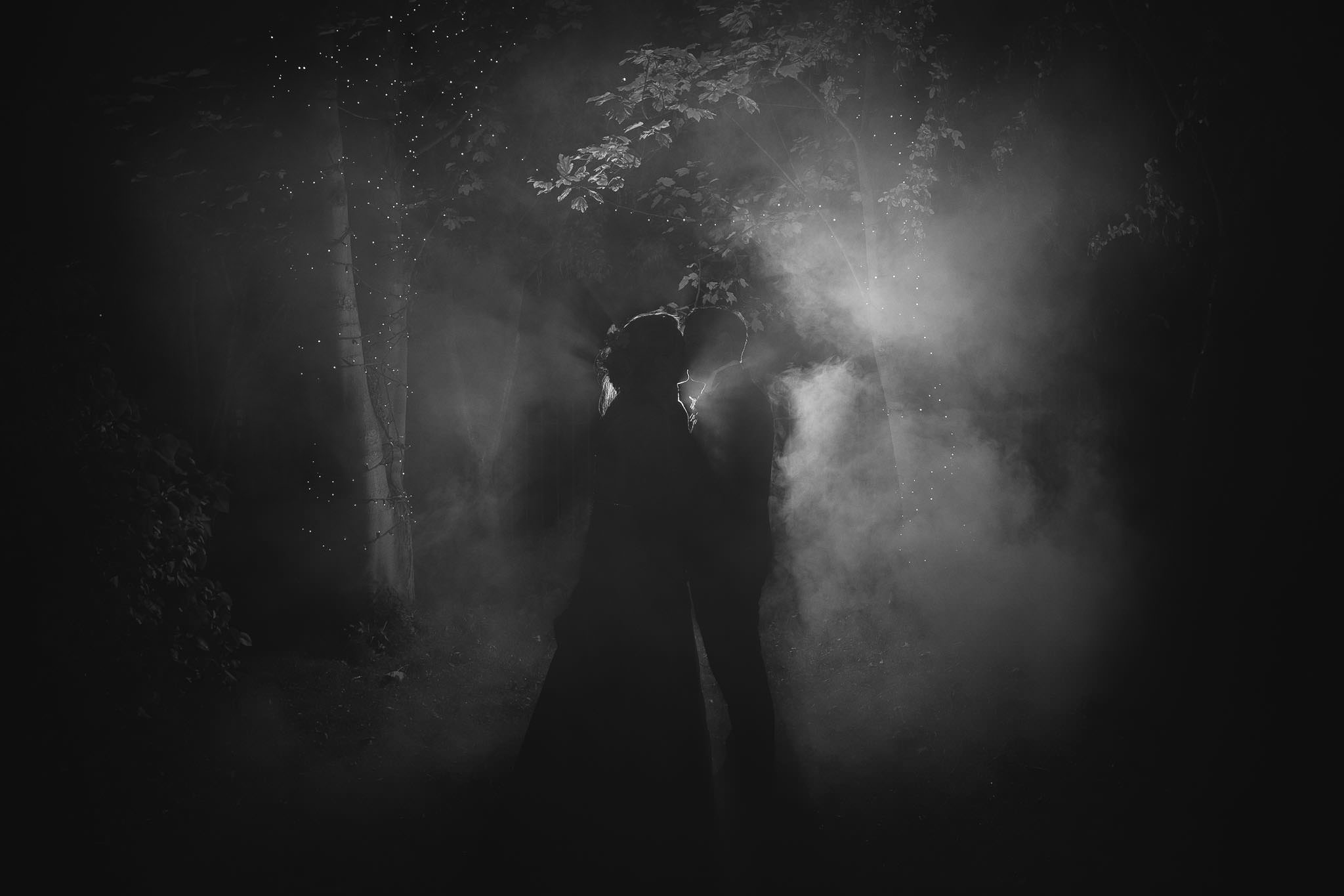 A romantic black and white photo of the bride and groom lit from behind through smoke