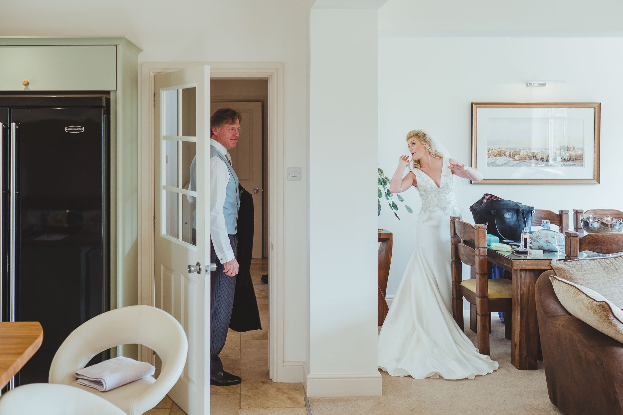 The bride checks herself in the mirror while a groomsman gets ready