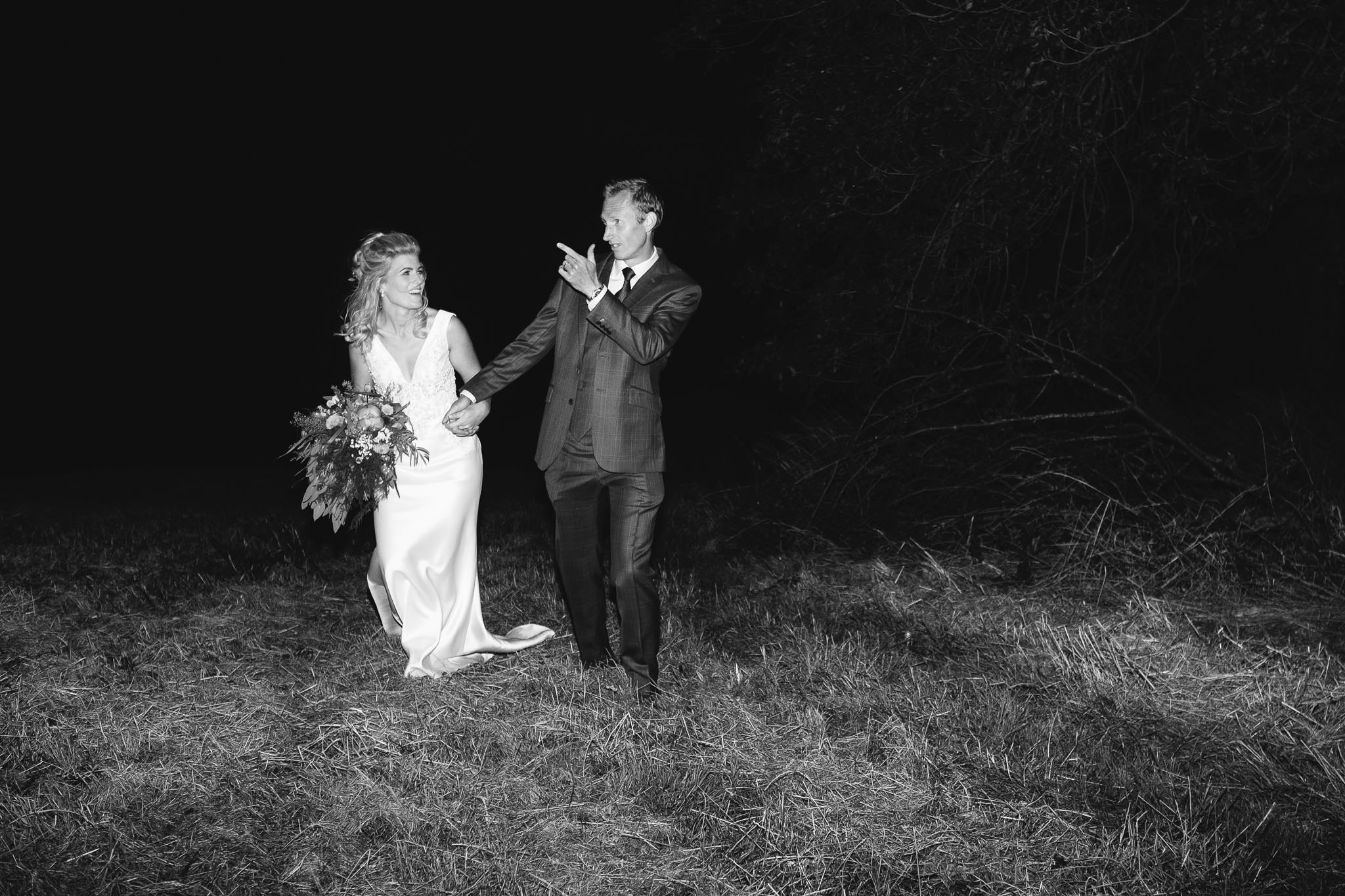 A black and white photo of the bride and groom pulling silly poses at night