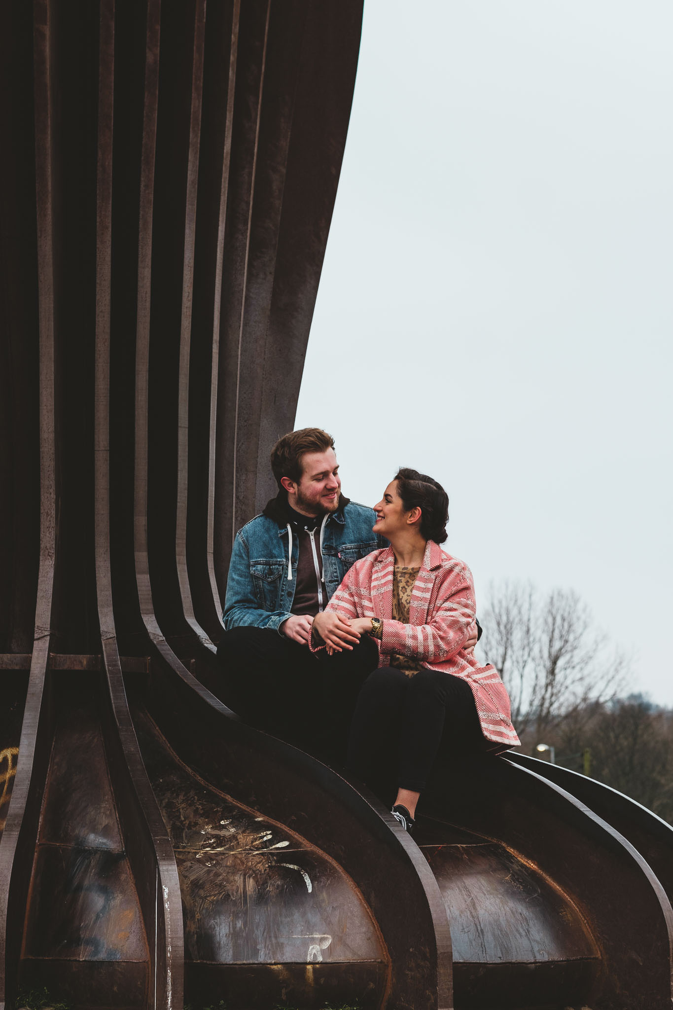 A close up of a couple laughing while sitting on the feet of the Angel of the North