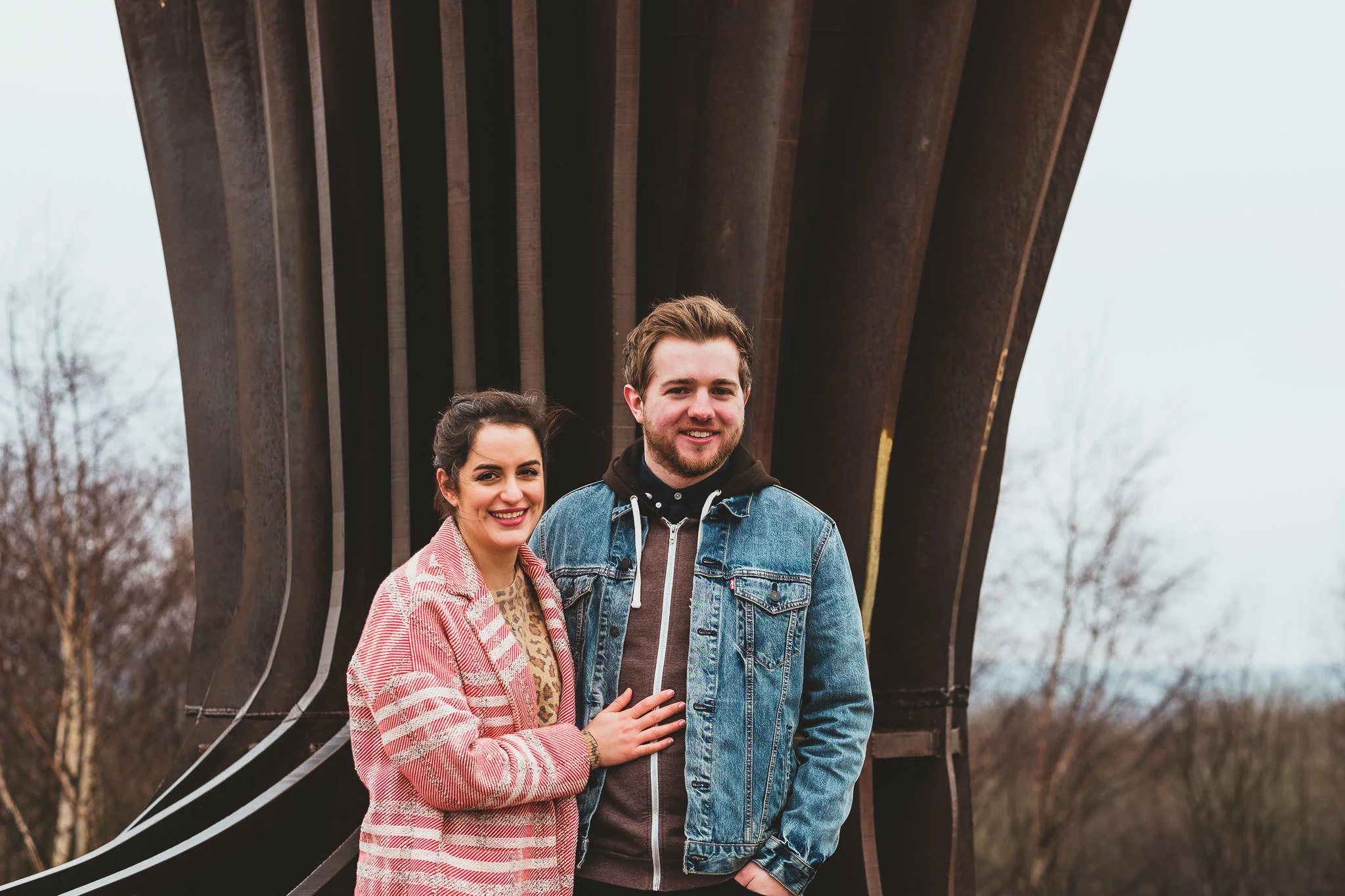 An engagement photo of a couple standing in front of the Angel of the North Gateshead