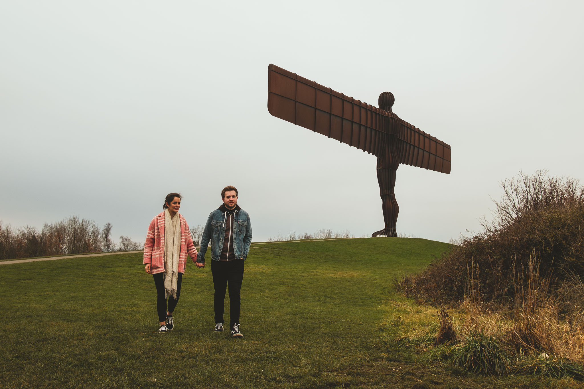 post wedding photo of a couple walking away from the Angel of the North while holding hands