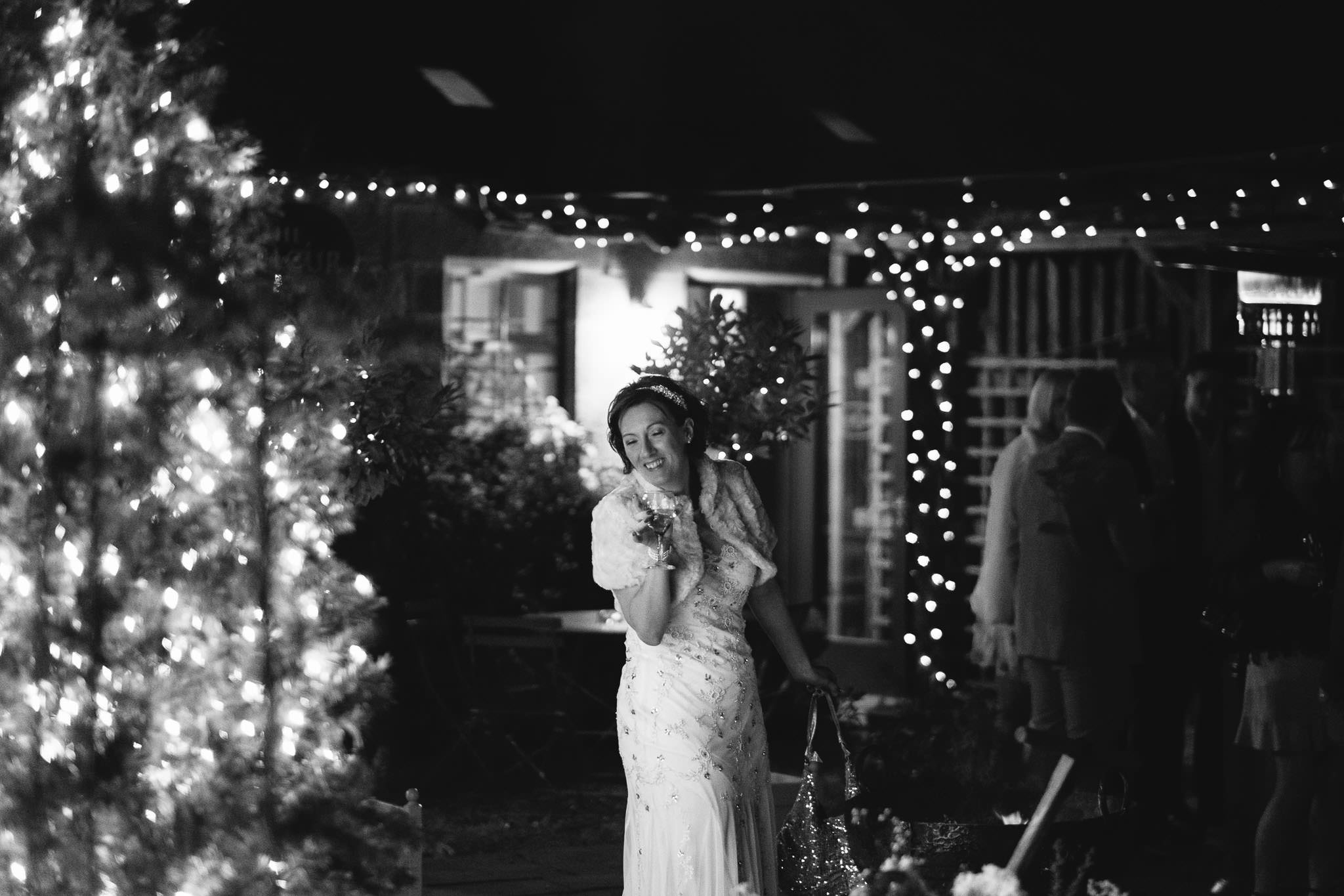 Black and white photo of bride pulling funny face with fairy lights behind