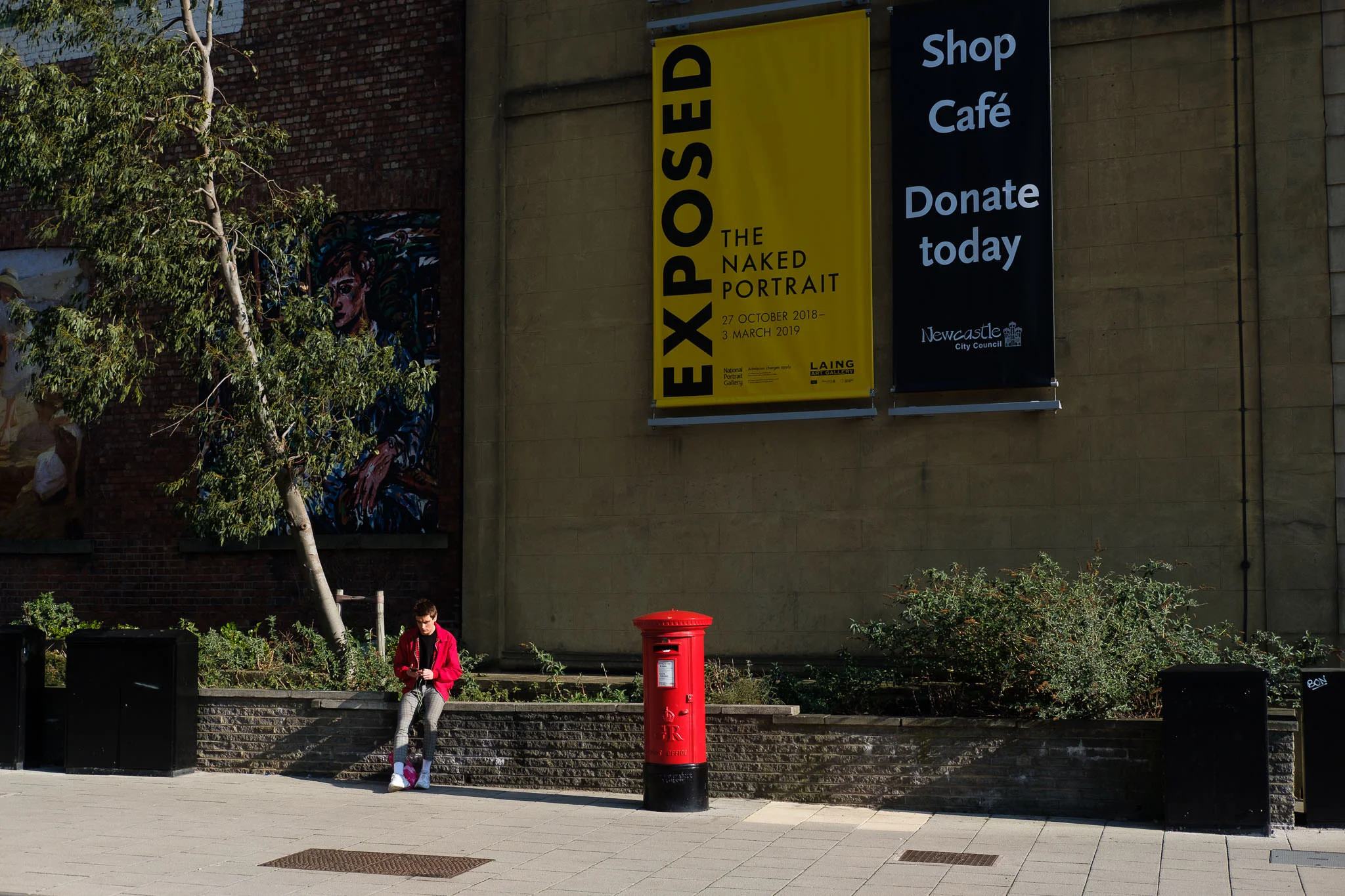Funny photo of a man in a red coat sitting next to a red post box