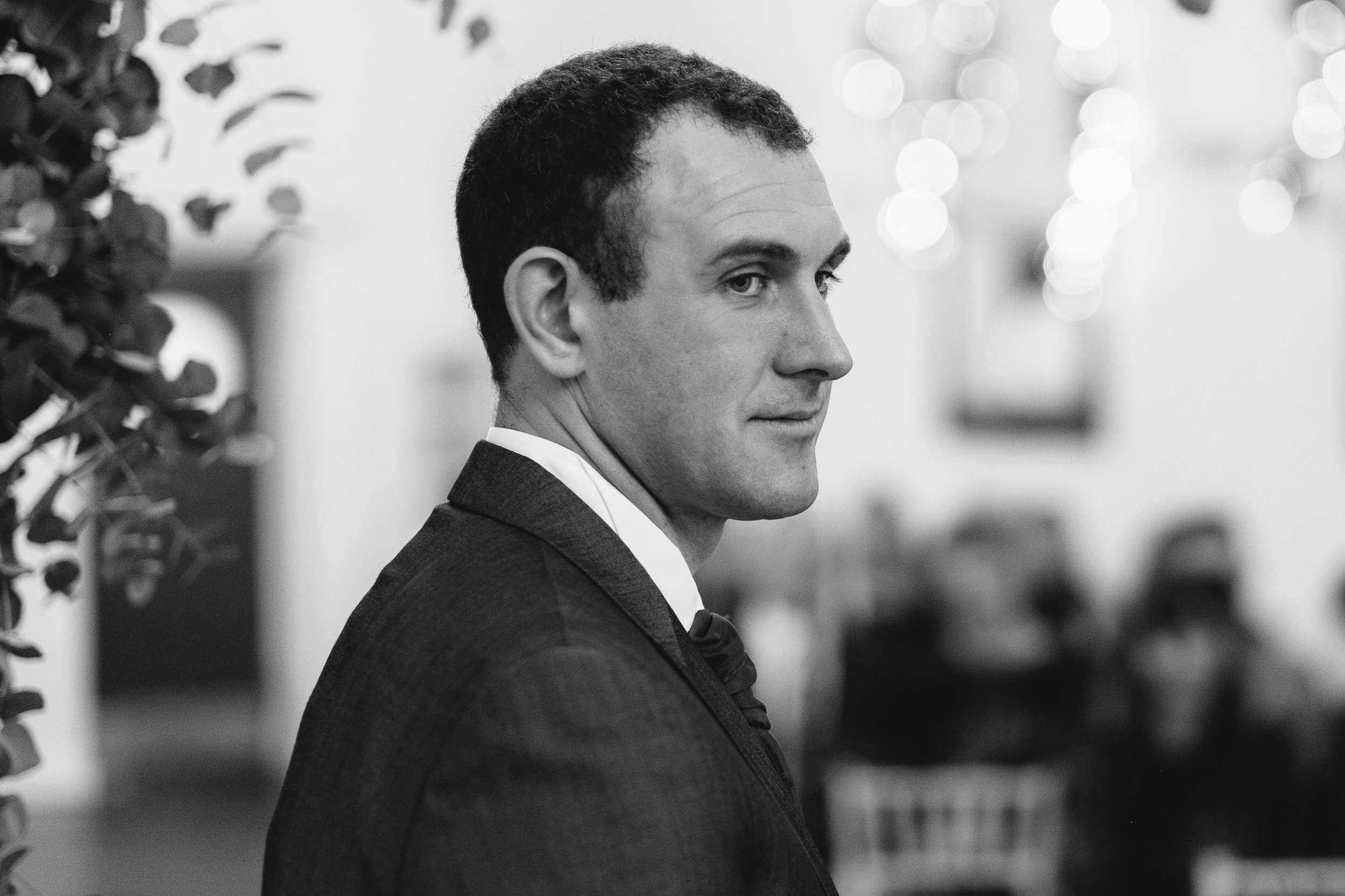 A black and white photo of the groom smiling during the wedding ceremony