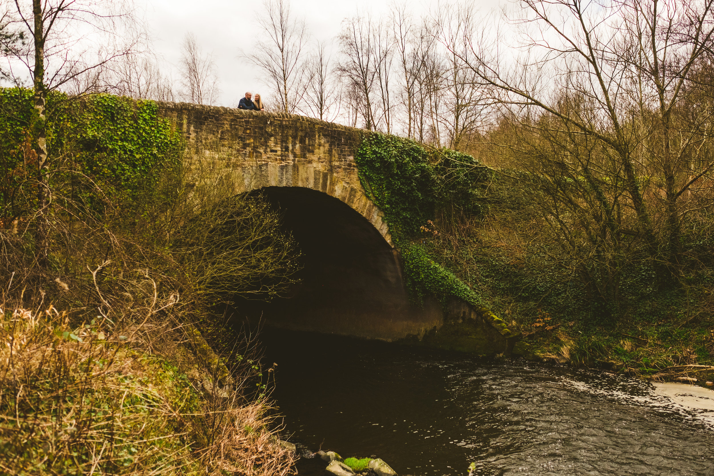Couple stand on hump back bridge with stream running underneath in Newcastle
