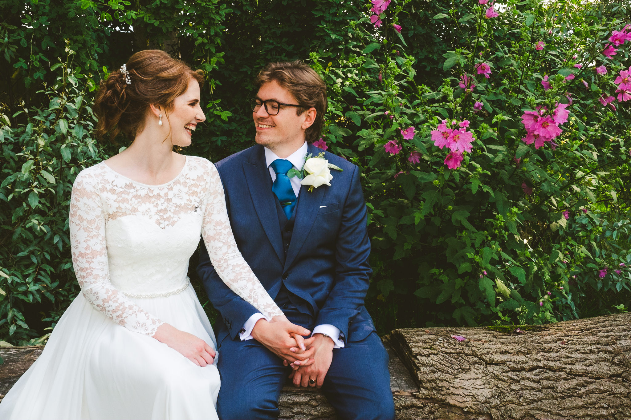 Close up of a bride and groom holding hands with flowers in the background