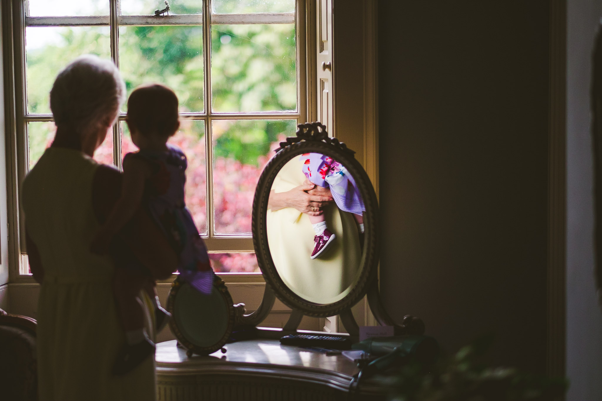 Mother of the bride holds the bride's daughter while looking out of the window