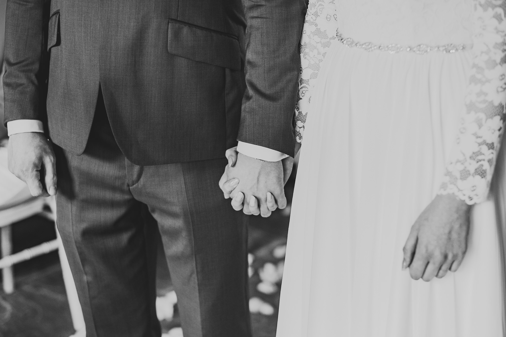 A black and white photo of the bride and groom holding hands during their wedding ceremony