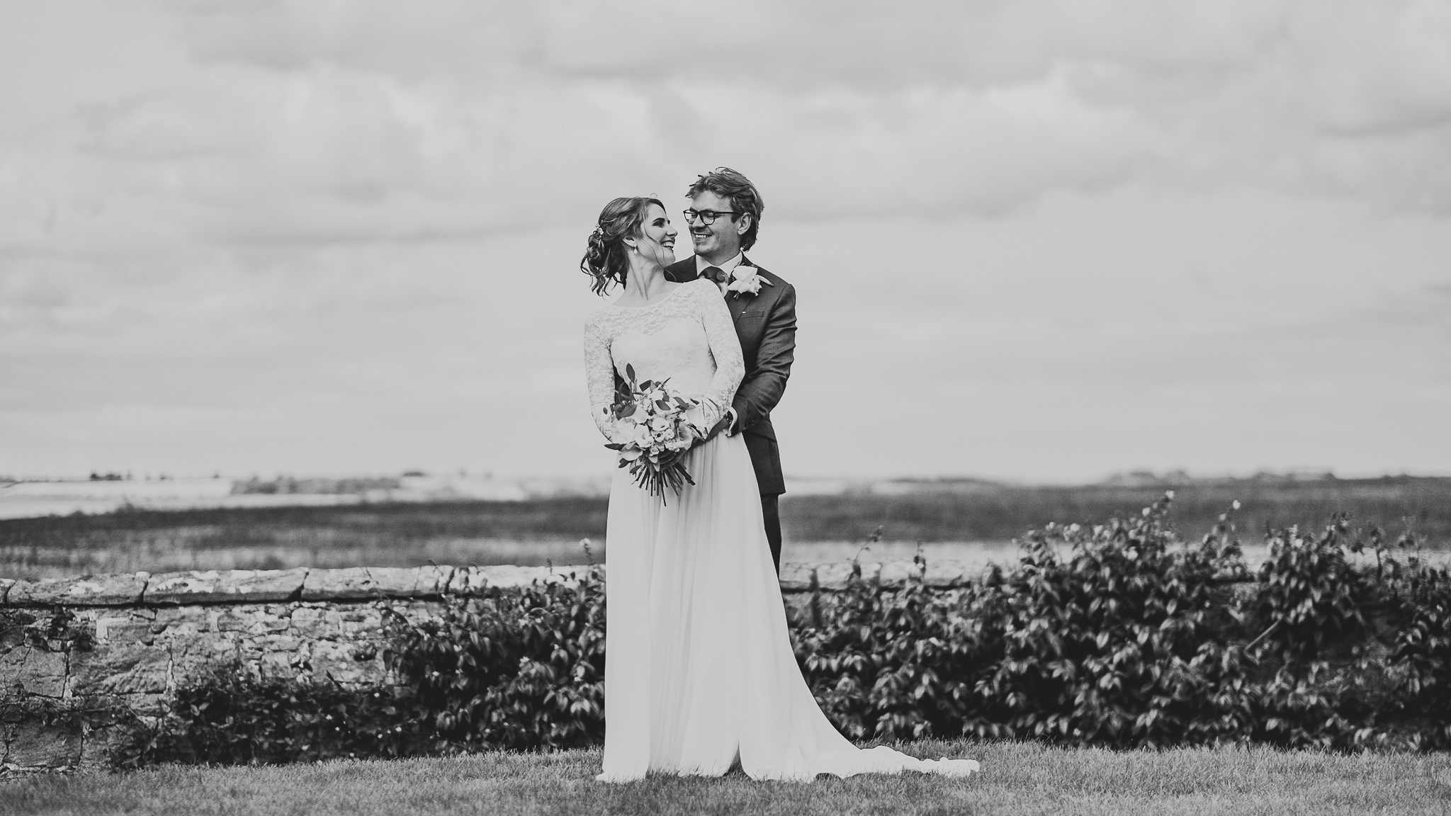 A black and white photo of the bride and groom cuddling with Northumberland countryside behind
