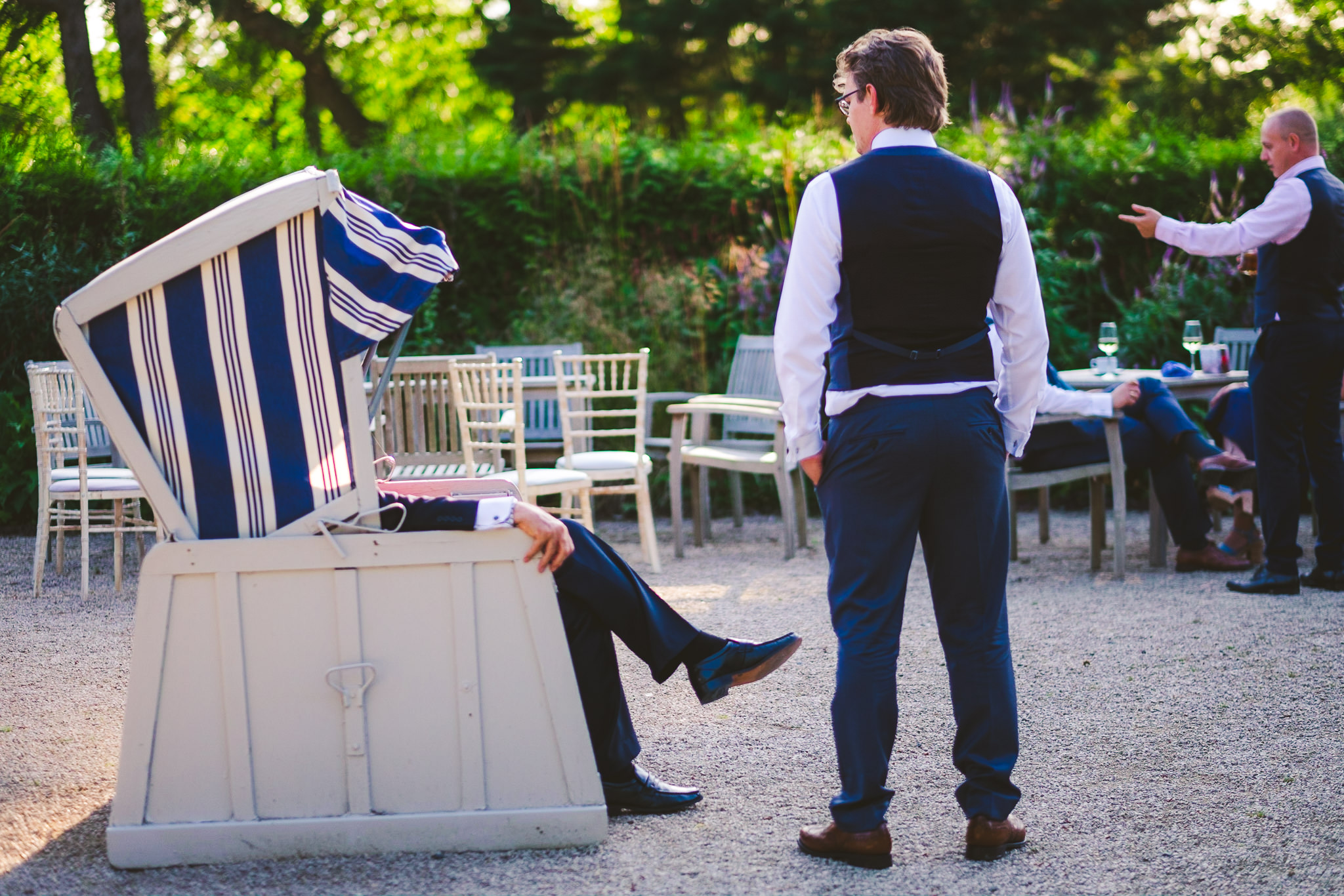The groom chats to a guest who is sitting in a fabric covered chair