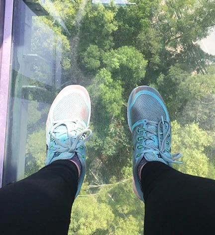Looking down at Lantau Island—and my filthy Nikes—while looking through the glass-bottom gondola on Lantau Island, China (©Deborah Clague, 2018). 
