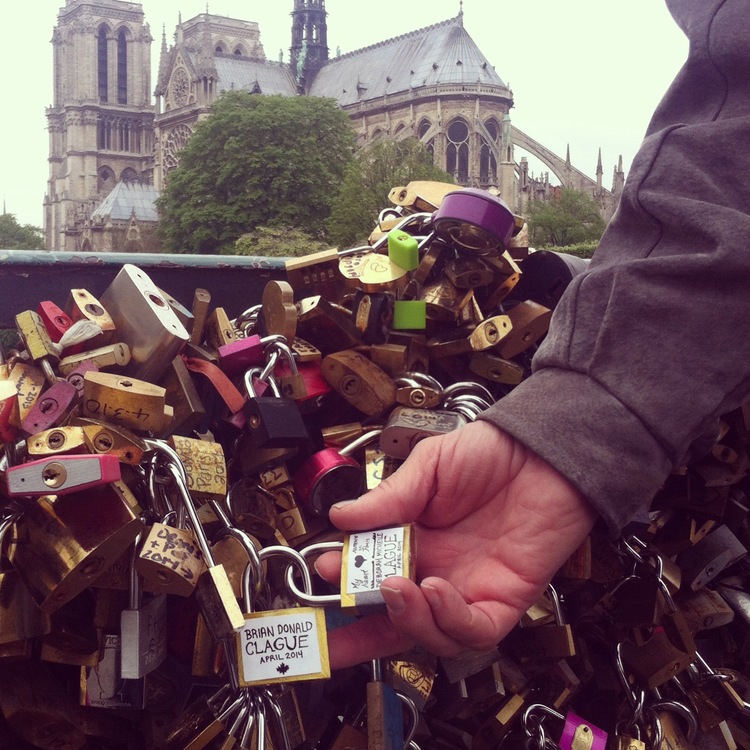 Intertwined locks for both my father and I placed on Pont de l’Archevêché, near Notre-Dame Cathedral visible in background, in 2014 (©Deborah Clague).