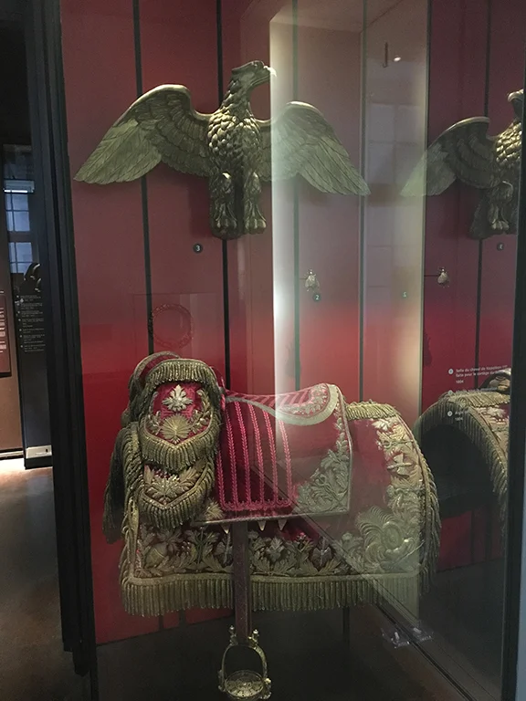 Napoleon’s insignia included an eagle with outspread wings (represented here from a bronze gilt from the First Squadron of the Regiment of Mounted Grenadiers of the Imperial Guard) and the saddle used on Napoleon’s horse during his coronation, Les Invalides (©Deborah Clague, 2019).