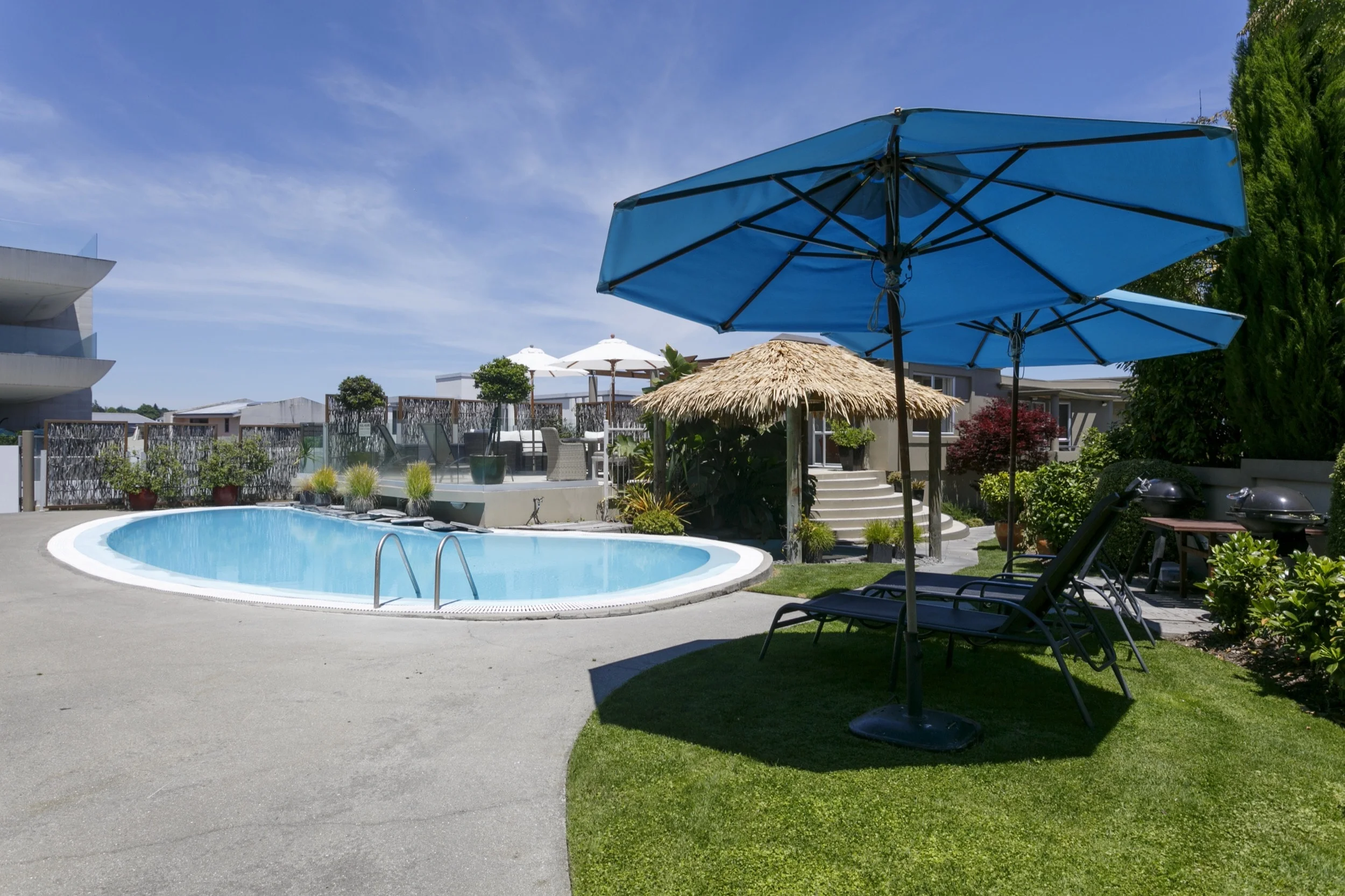 Pool area showing heated pool and sun loungers and BBQ with patio area behind -min.jpg