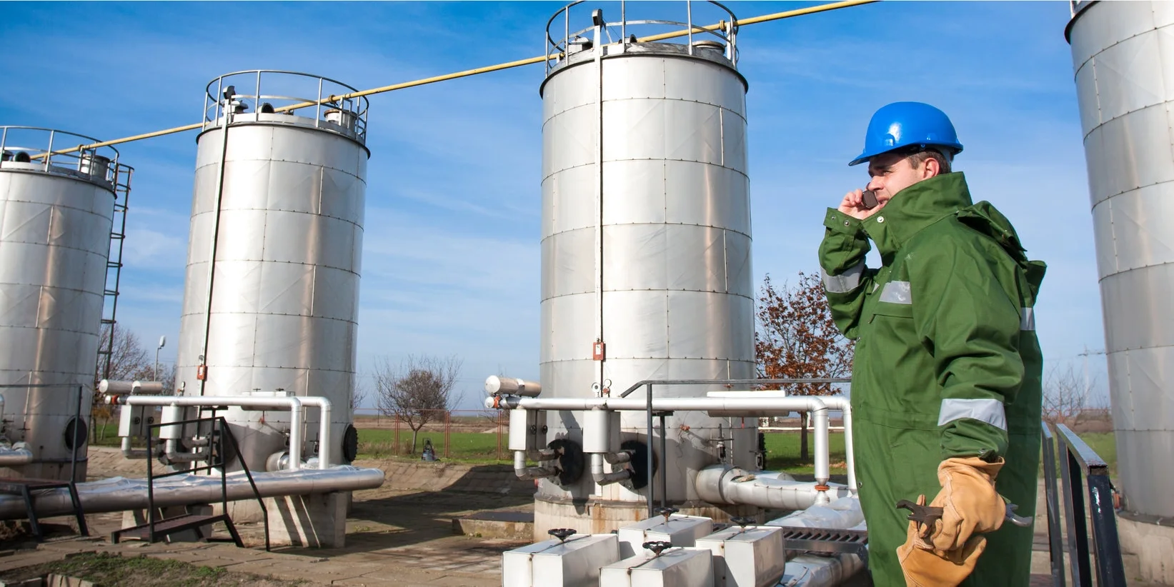Oilfield Operator talking on phone in front of tanks