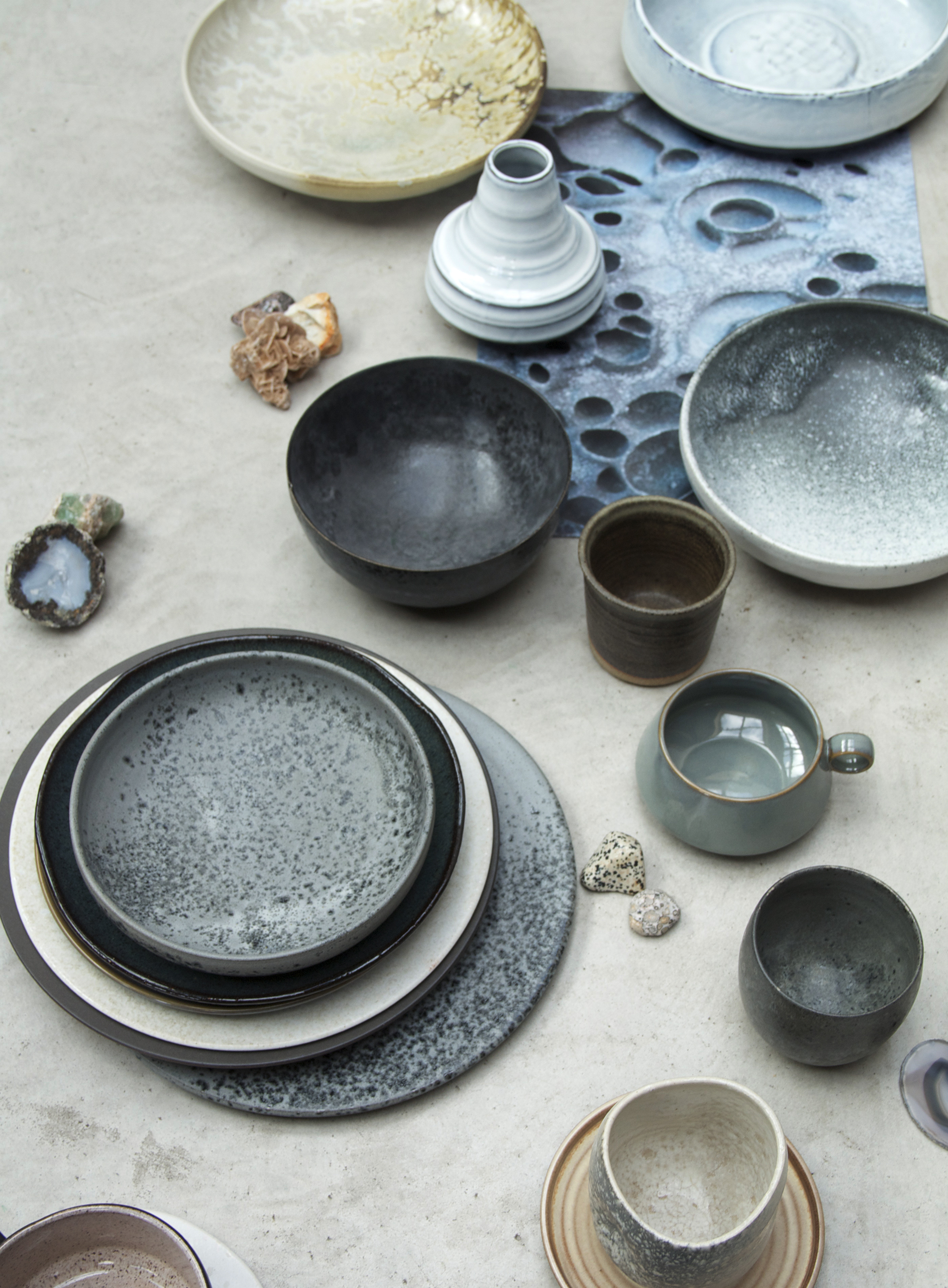 Servies van links naar rechts, van boven naar beneden: Aardewerk bord van KH Wurtz , witte schaal van HK Living , Vaas wit HK living , Edelstenen via , Zwarte schaal via KH Wurz, wit/zwarte schaal via KH Wurtz , Donkerbruin potje van StyleCookie propshop, Stapel borden van KH Wurtz, Blauwe kom van Ferm Living , Antraciet mok KH Wurtz , Ecru mok van KH Wurtz op een schoteltje van StyleCookie propshop