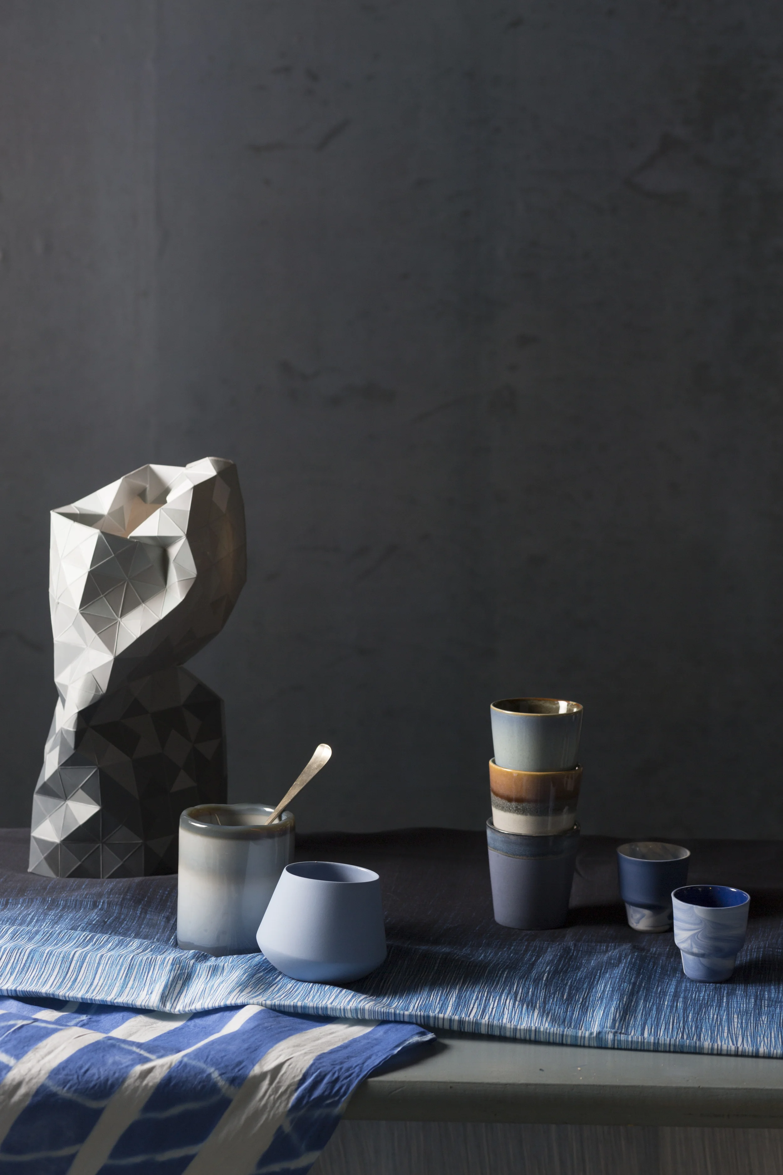 Tafelkleed van Ferm Living , Vaas 'Papervase' via Store without a Home , Potje met (eigen) lepel 'HK Living' via Villa Jipp , Licht blauw potje van Elke van Den Berg , Stapel bekers 'HK Living' via Villa Jipp , Bekers van 'Alissa en Nienke' via Restored