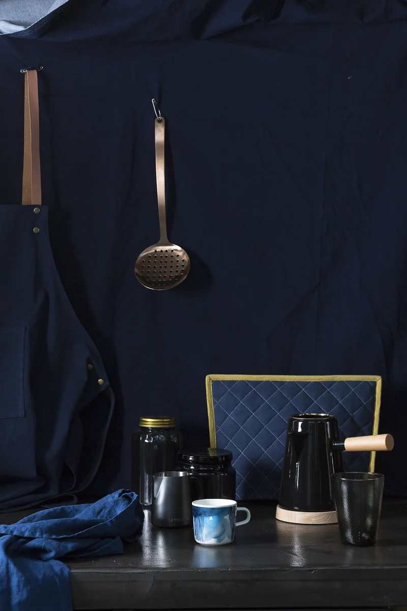 Tafelloper van H&M Home , Glazen voorraadbus met gouden deksel van H&M Home , Melkkannetje van &Klevering , Glazen voorraadpot van H&M Home , Beker met blauwe verf motief 'Marrimekko' via &Klevering , Koffiepot van Restored, Glas van &Klevering , Theemuts van Ferm Living , Schort van Ferm Living , Opscheplepel van Hema