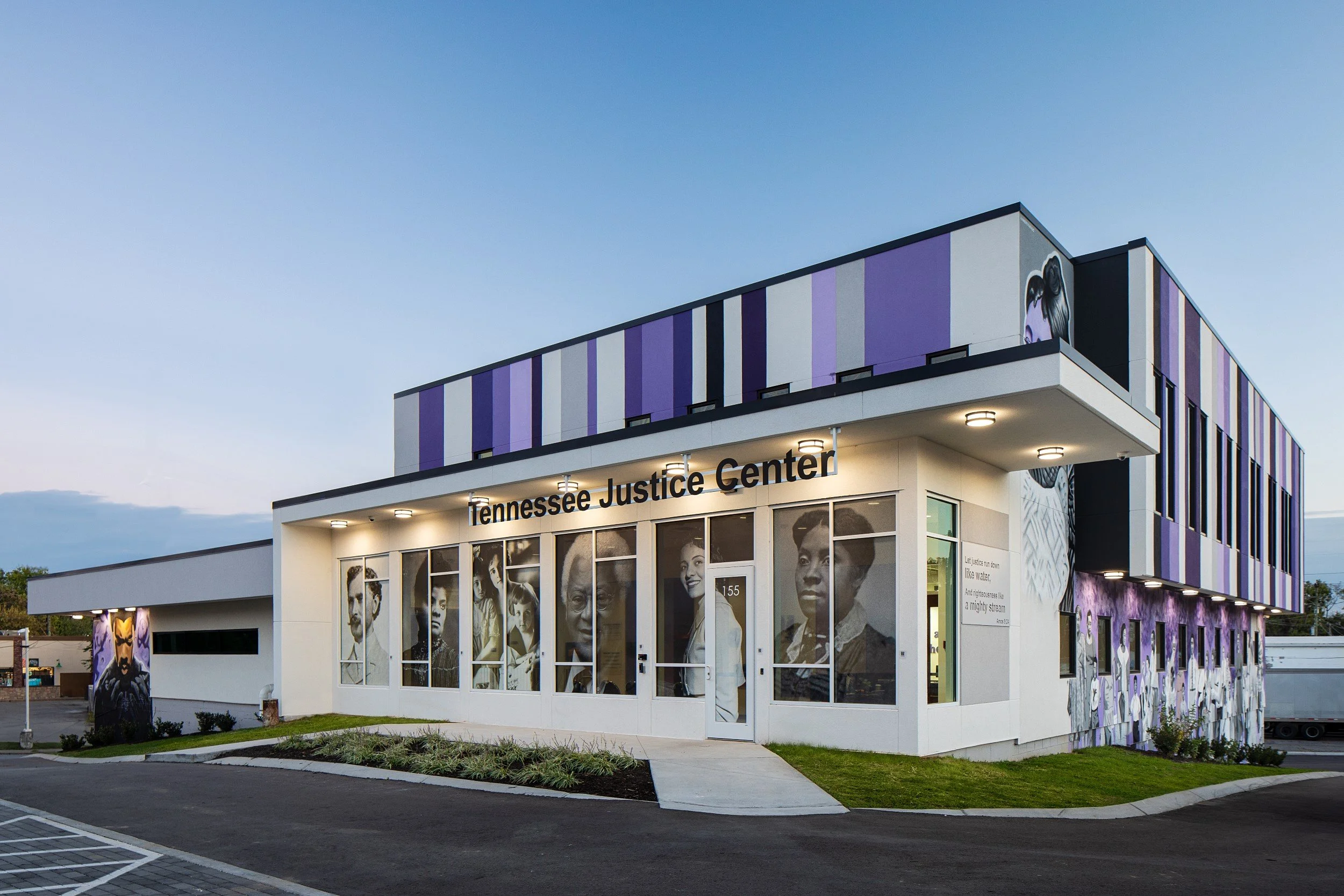 The Tennessee Justice Center building with black and white historical photographs of diverse individuals on the front windows and purple striped accents on the upper exterior wall, under a clear evening sky.
