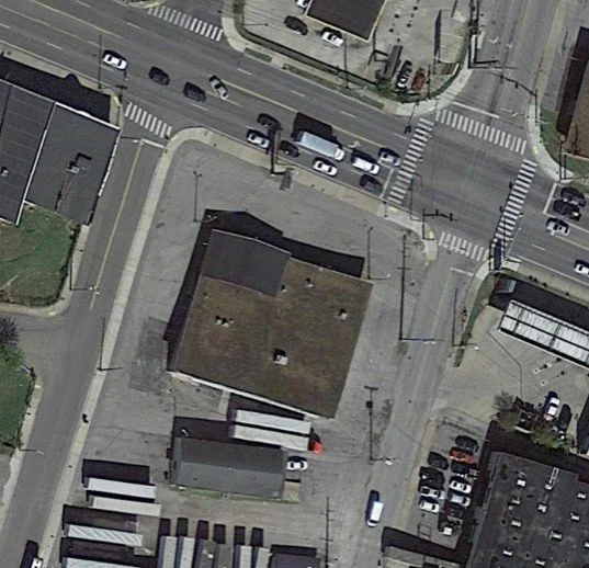 Aerial view of a city block showing a large building, parking lot, and surrounding streets with cars.
