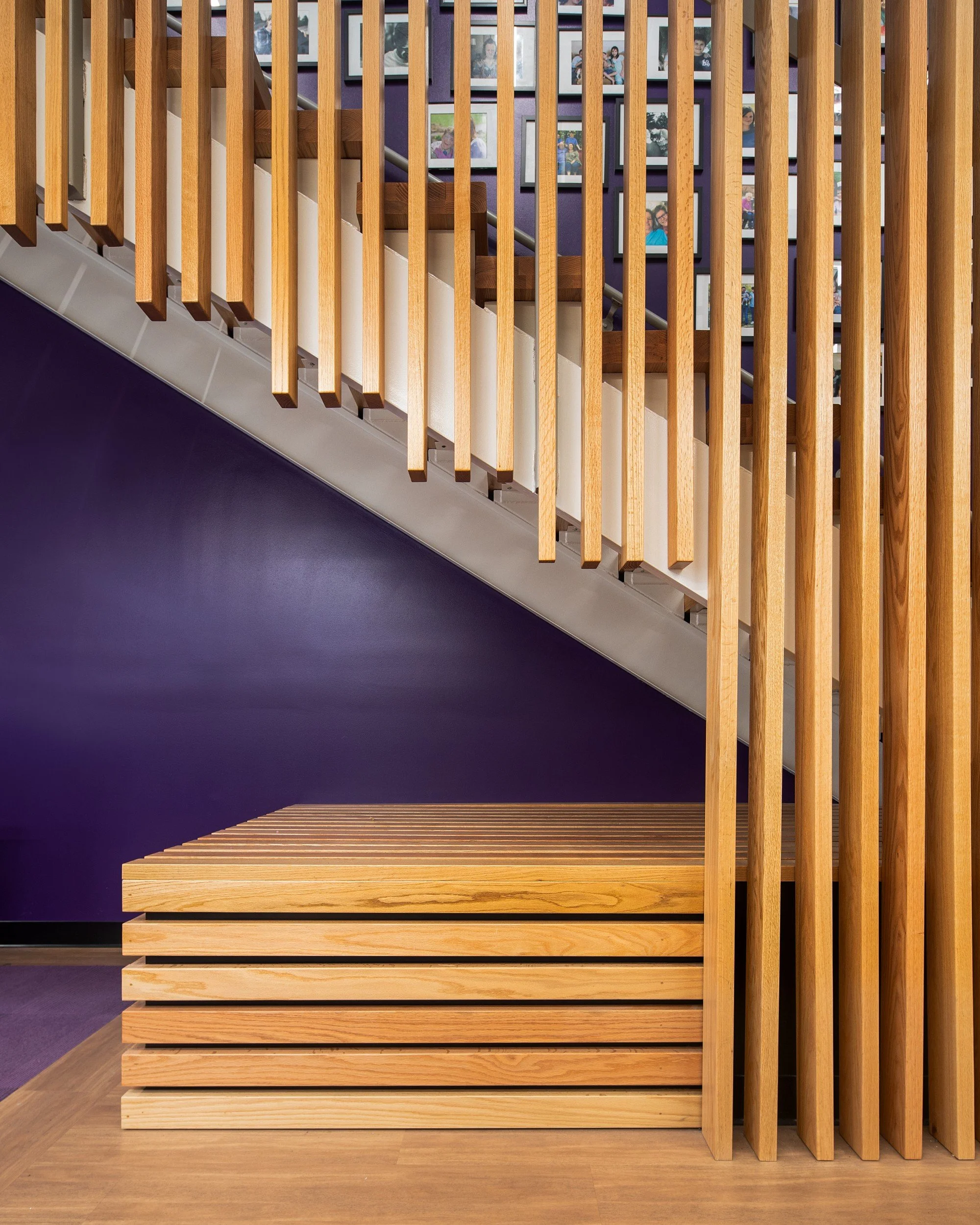 Wooden staircase with vertical slats and purple wall covered with framed photographs