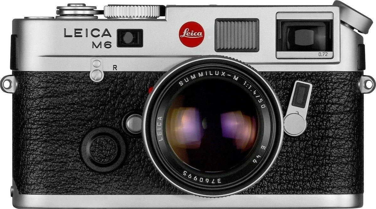 A vintage Leica M6 rangefinder film camera with silver top and bottom, black textured body, and various buttons and dials, featuring a Leica Summilux-M 50mm lens attached.