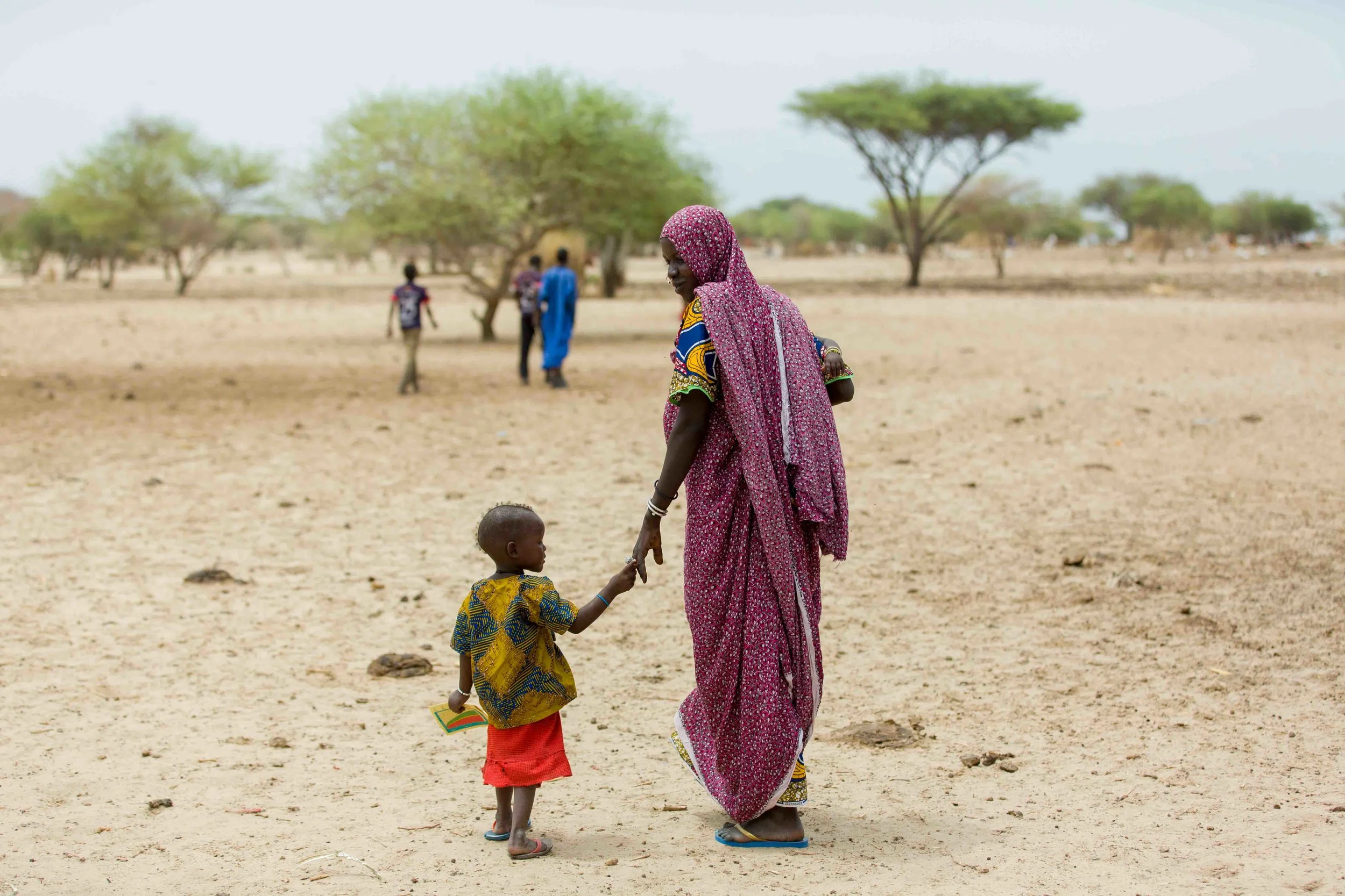  A little girl clutches her immunization card as she walks with her mother and sibling after a vaccination session. The children, part of a nomadic community, received routine vaccinations, during an outreach session. Mafou, Bol District, Chad.  