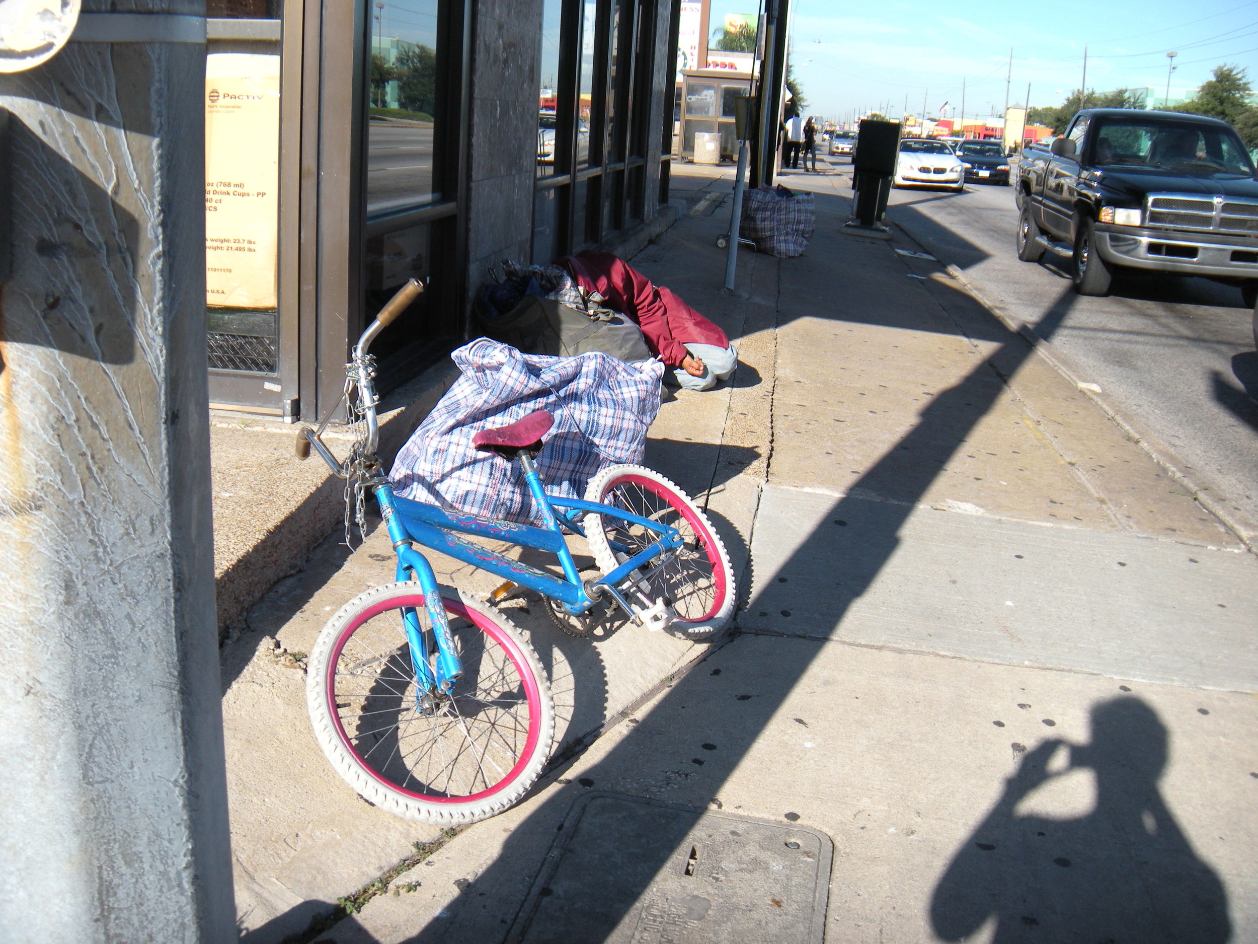There's a person asleep in there. This mound of possessions represents the belongings of all the people who are working the corner, not just the one who is sleeping. Whose shadow is that? 