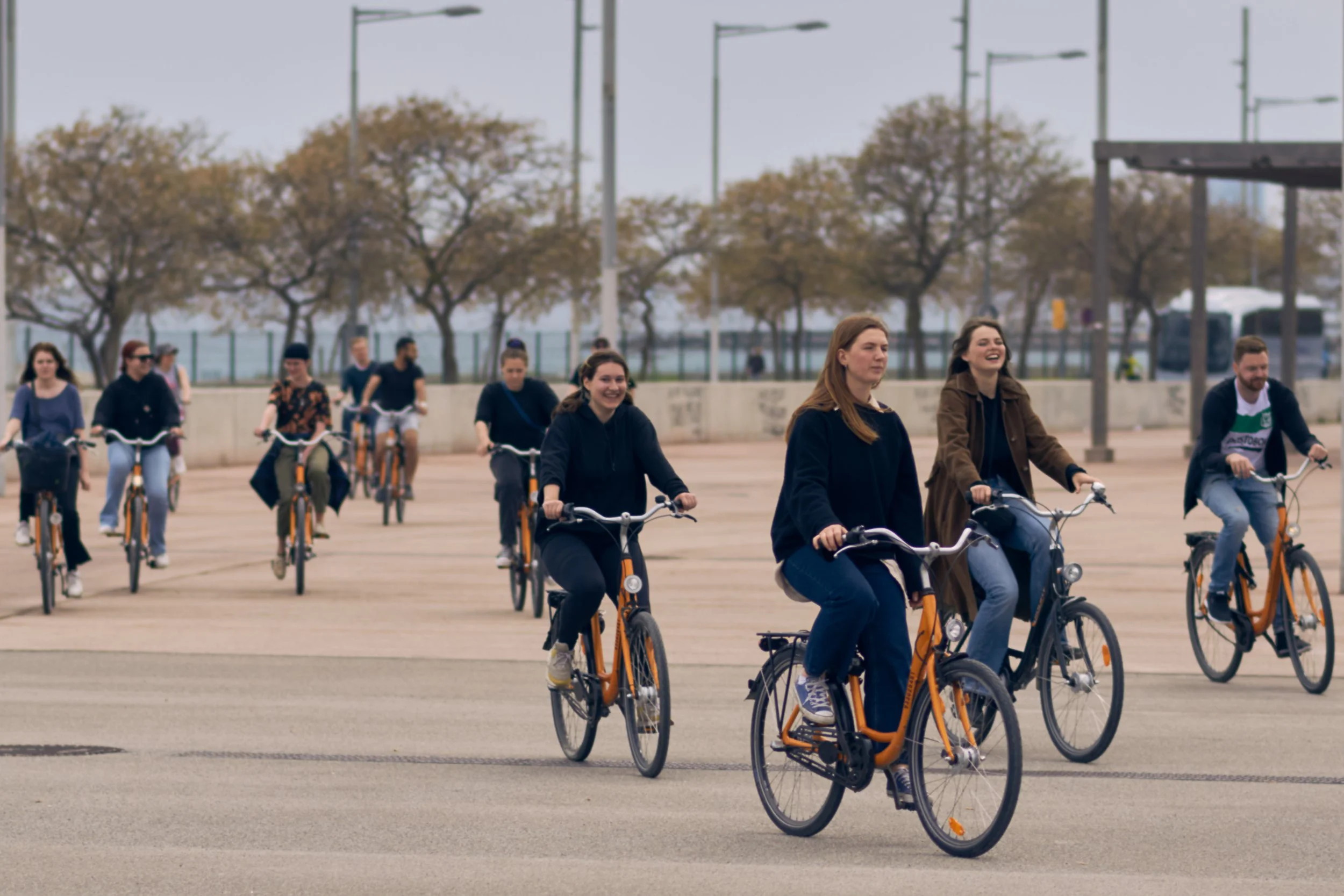 Flera personer som cyklar tillsammans på ett öppet område, med träd och en mur i bakgrunden.