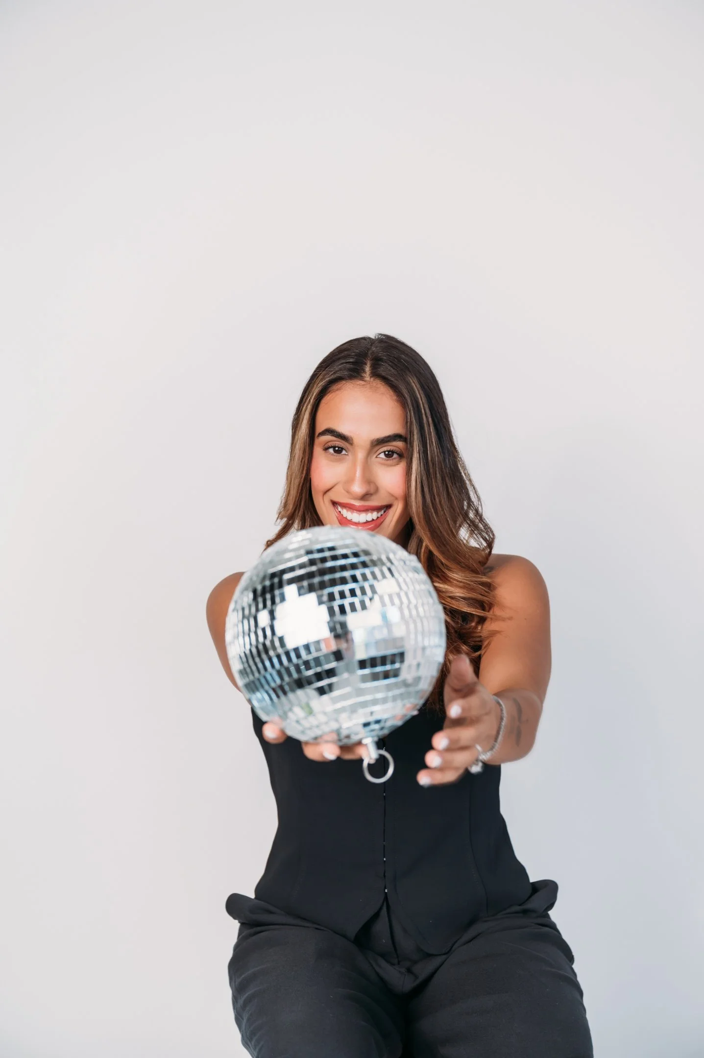 Smiling woman in black outfit holding a disco ball in front of a plain white background. Alisha Mowry Photography Military, Brand, and Portrait Photographer San Diego CA