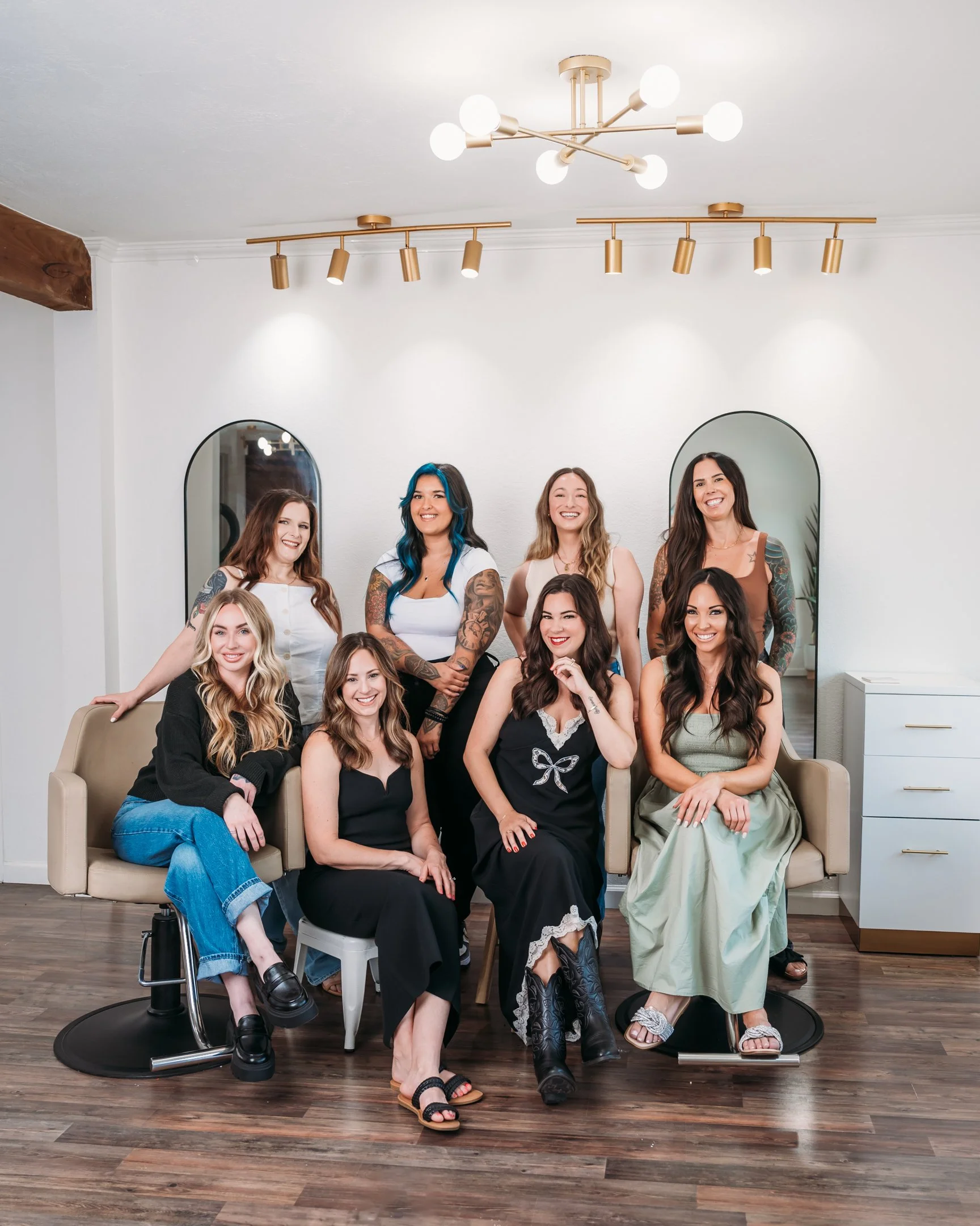 A group of eight women with diverse hair colors and styles, some with tattoos, posing inside a modern salon with mirrors and contemporary lighting fixtures. Alisha Mowry Photography Military, Brand, and Portrait Photographer San Diego CA