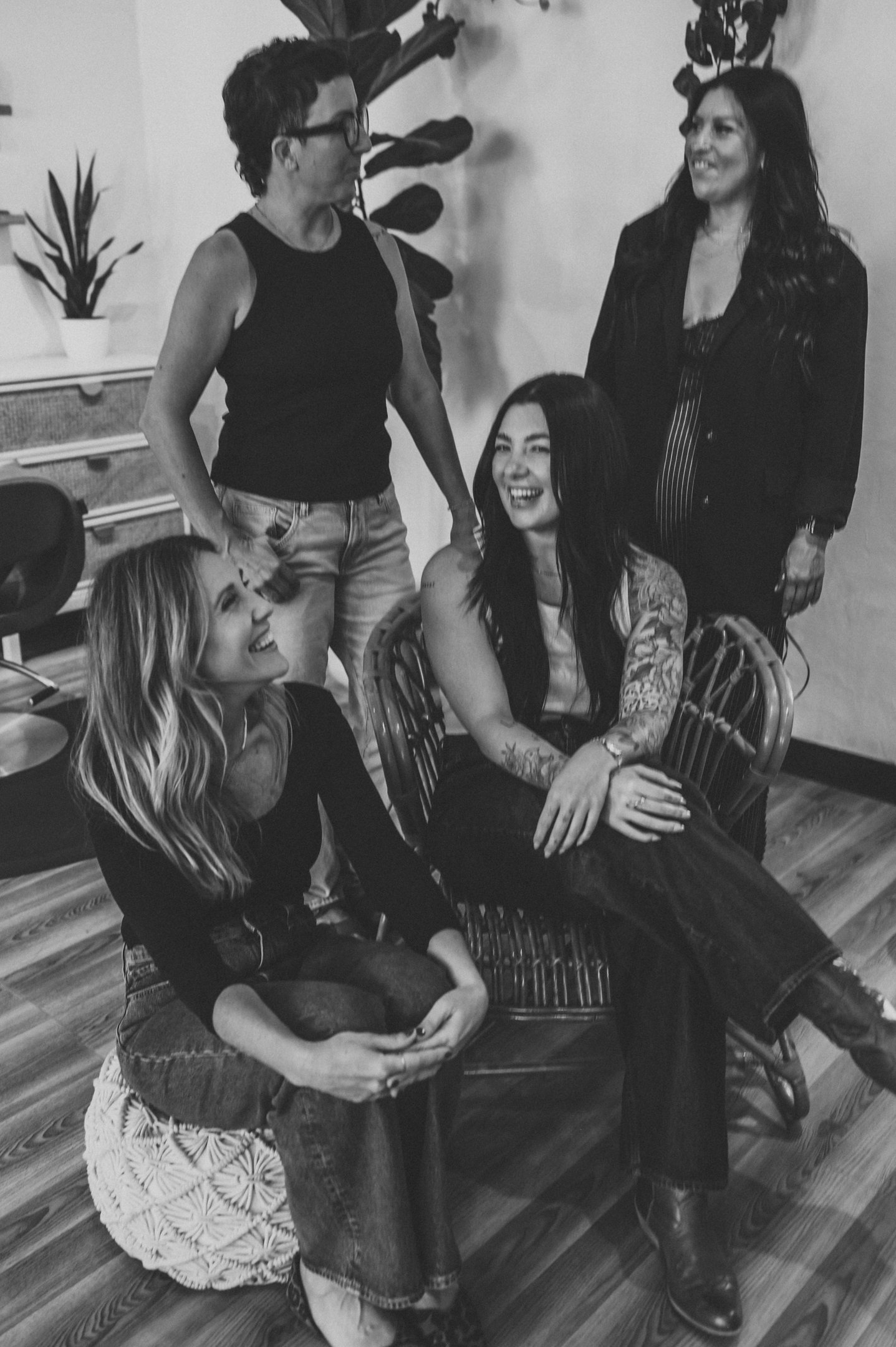 Five women in a room, some sitting and some standing, engaged in conversation and smiling, with potted plants on the wall. Alisha Mowry Photography Military, Brand, and Portrait Photographer San Diego CA