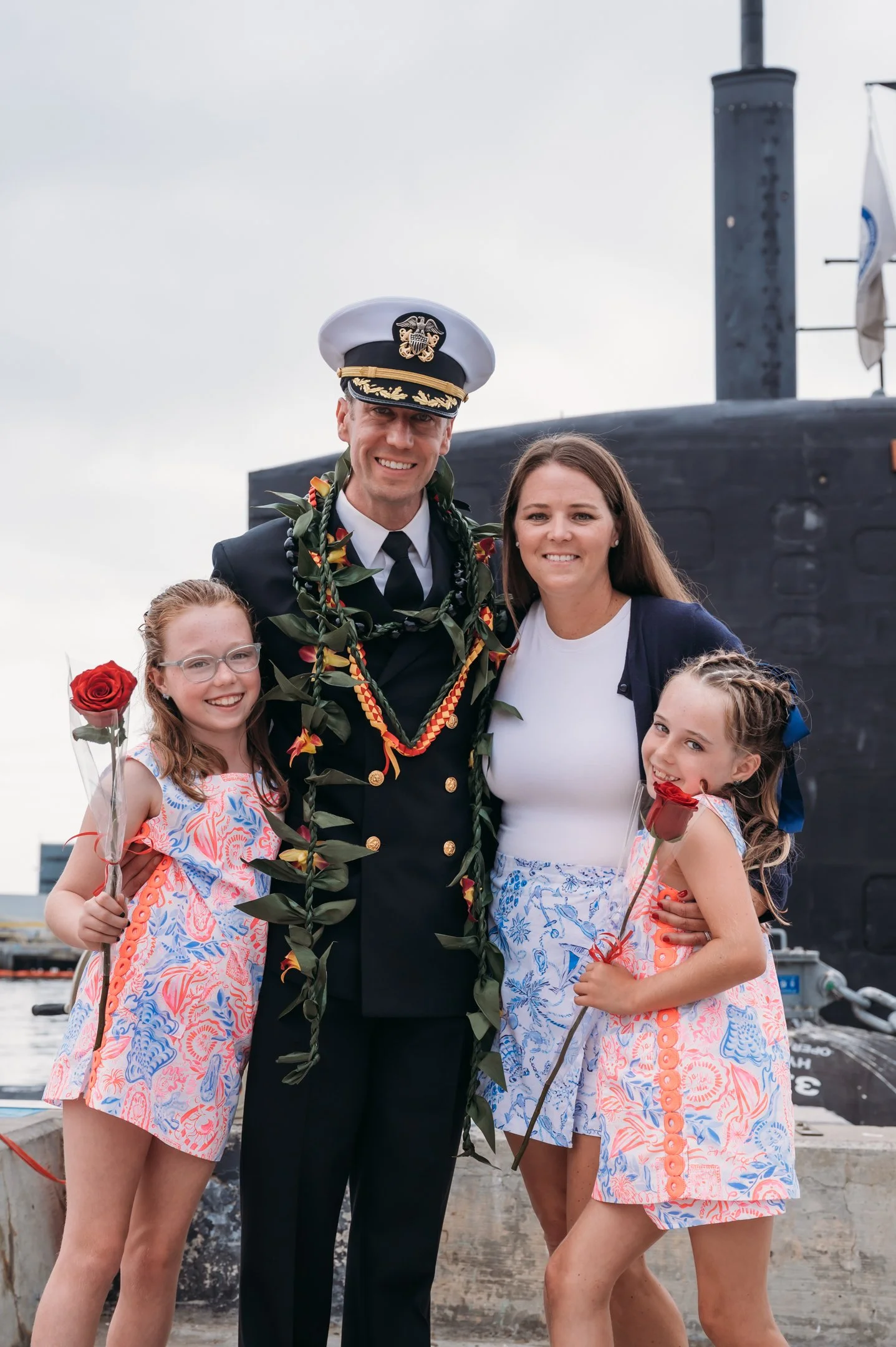 A man in naval uniform with two women and two girls, all smiling and holding roses, standing in front of a submarine. Alisha Mowry Photography Military Photographer San Diego