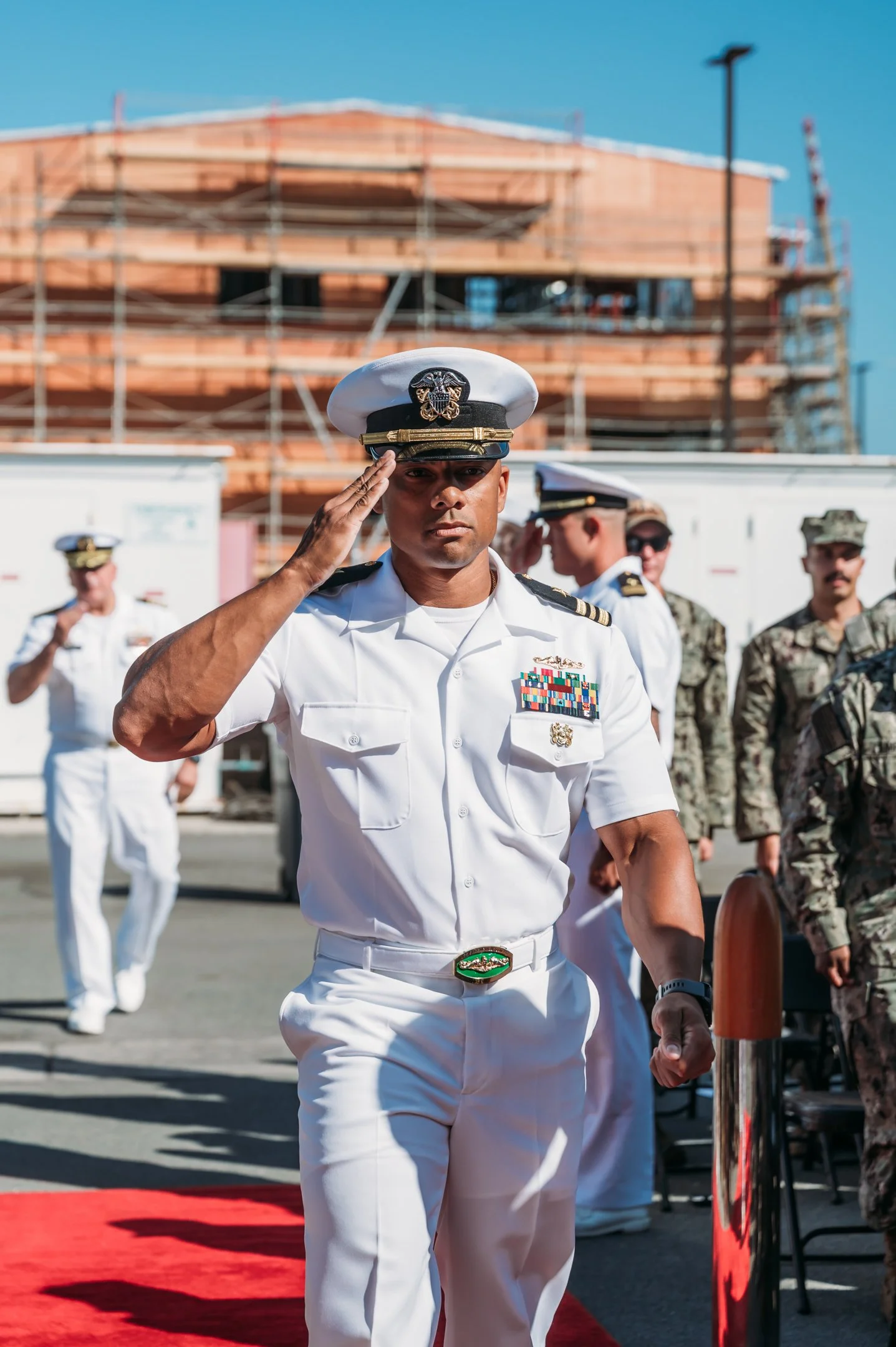 A military officer in white uniform saluting during a ceremony, with other military personnel in uniform. Alisha Mowry Photography Military Photographer San Diego